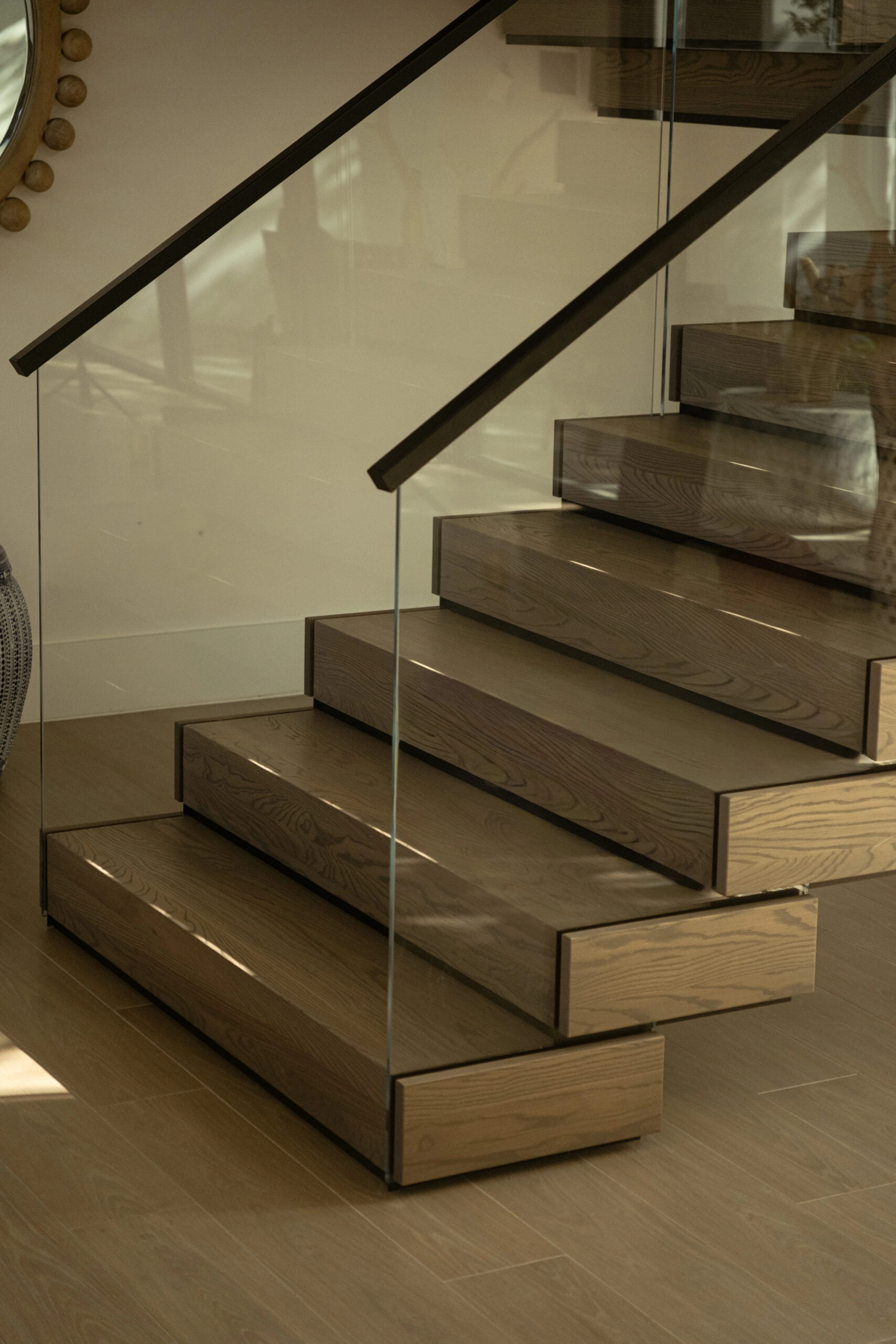 Lower stacked treads meeting the floor behind a frameless glass panel