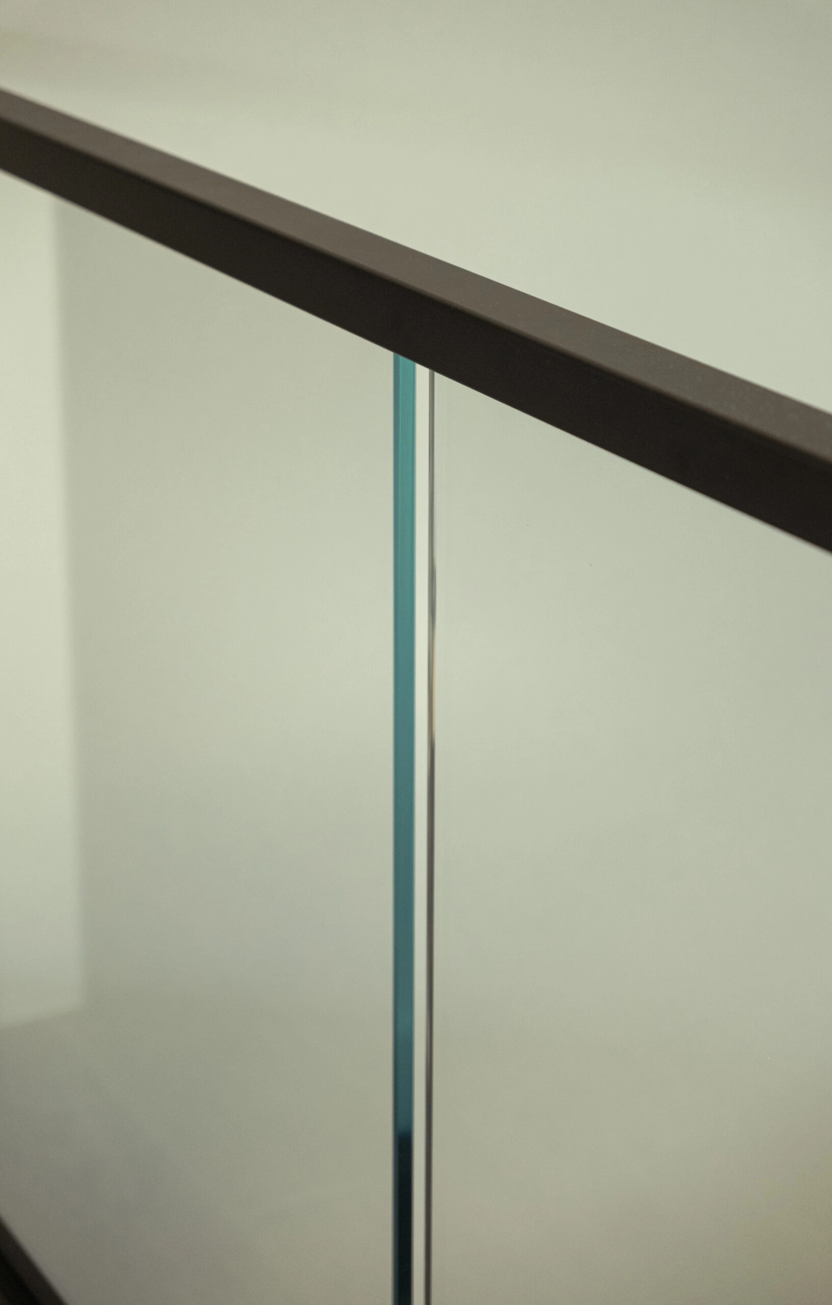 Close detail of the joint between two glass panels under a dark cap rail
