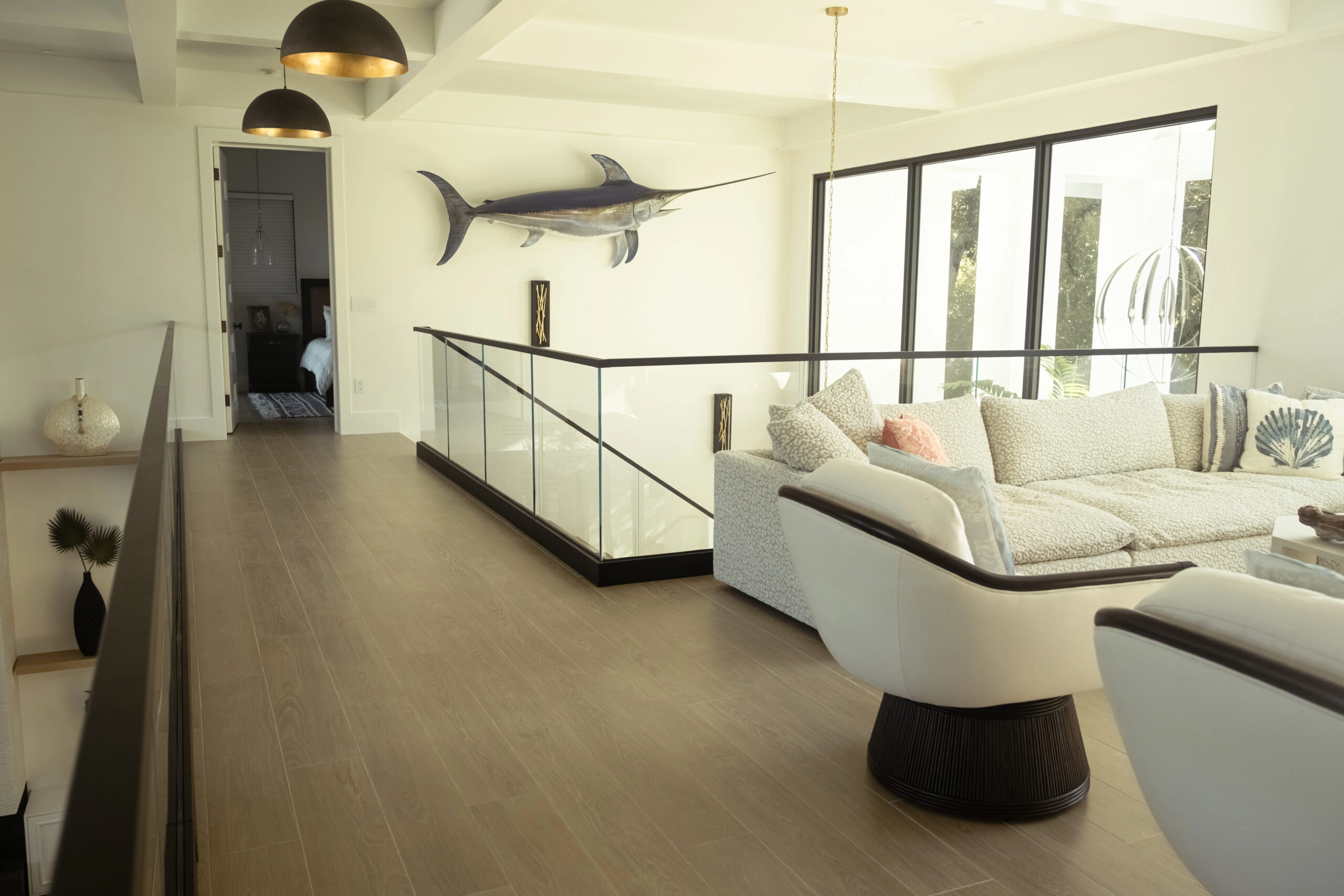 Upper living area edged by glass railing with a mounted sailfish on the wall