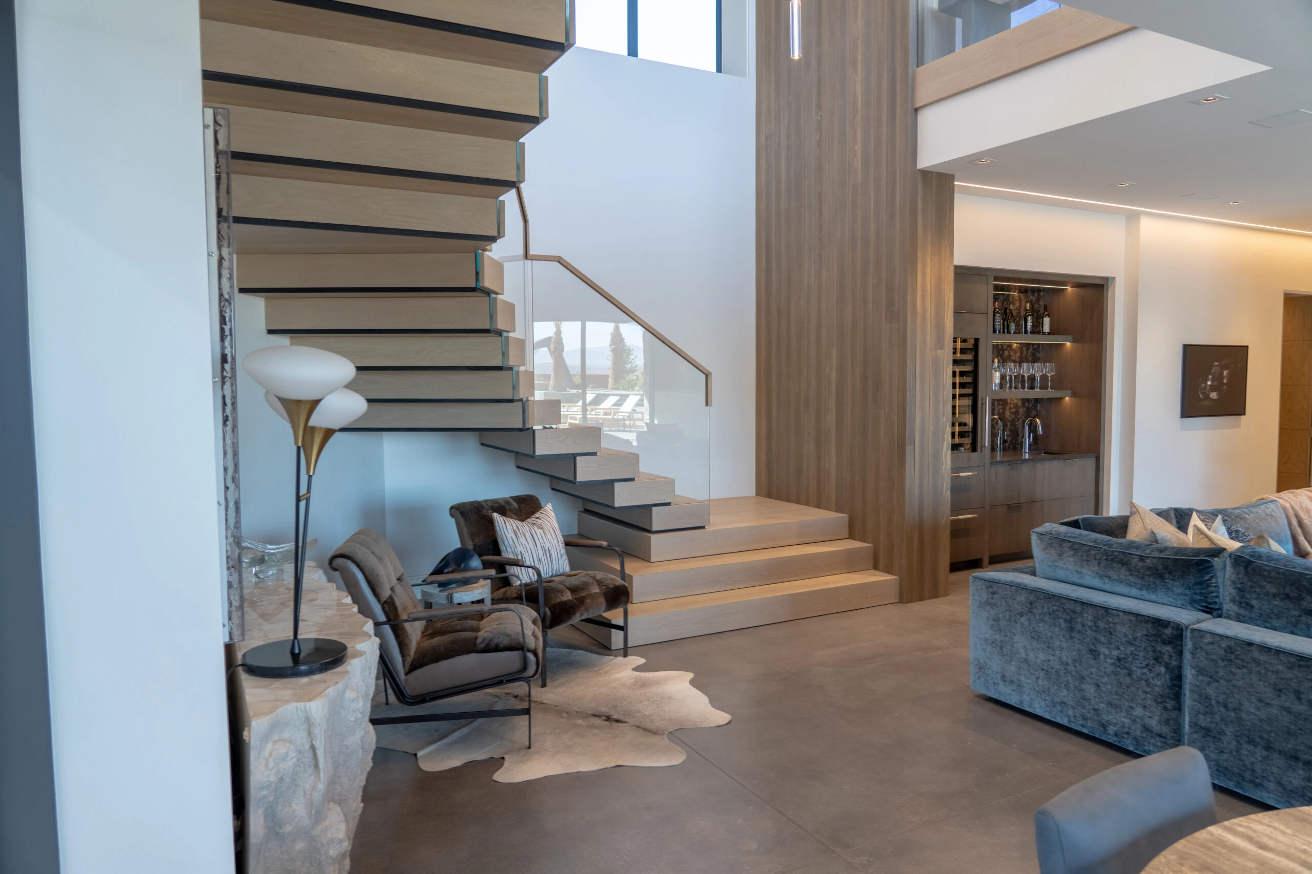 Open living room with the pale stacked stair and glass railing along one wall