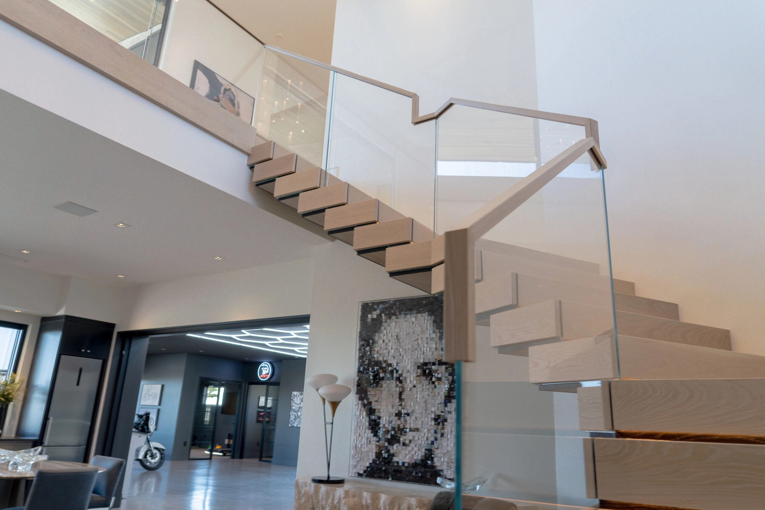 Stair and upper balcony wrapped in glass railing above a large portrait artwork