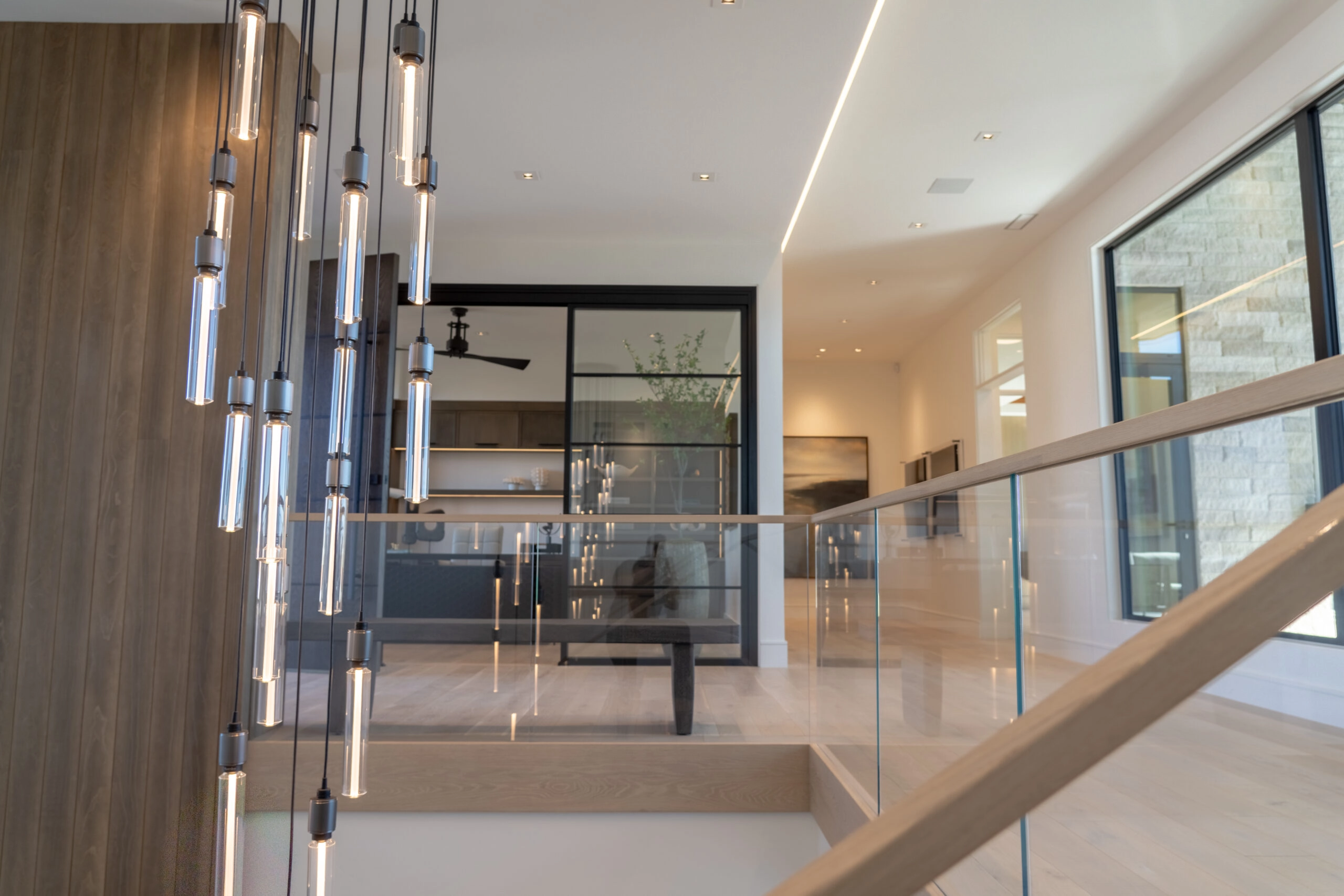 Pendant lights hanging beside the glass railing that edges the stair opening