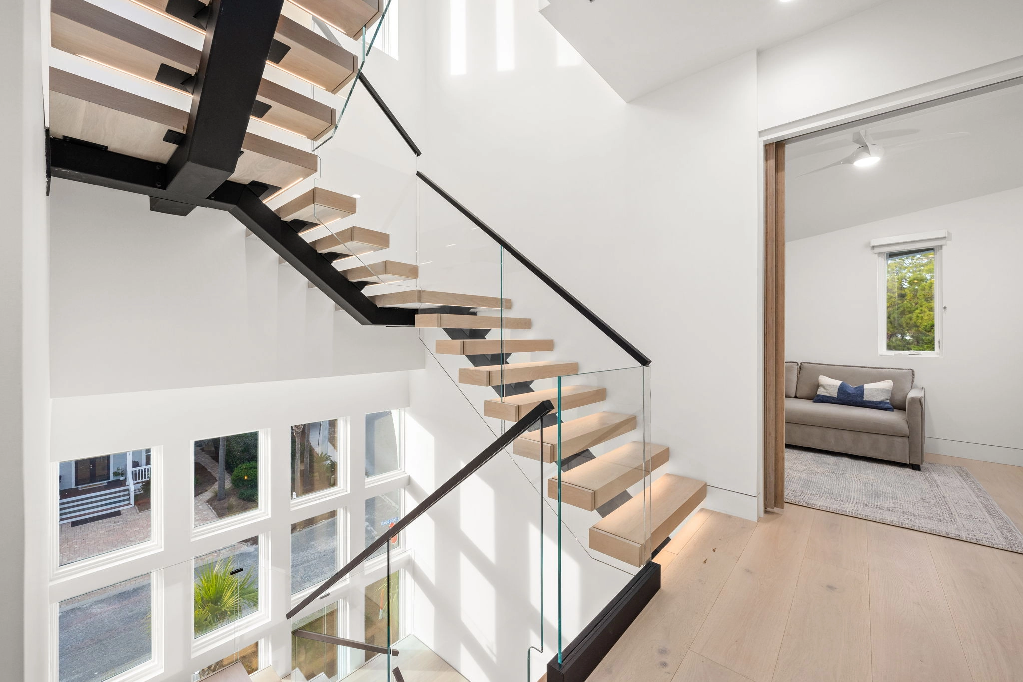 Floating stair with wood treads, black center stringer and glass railing beside a landing