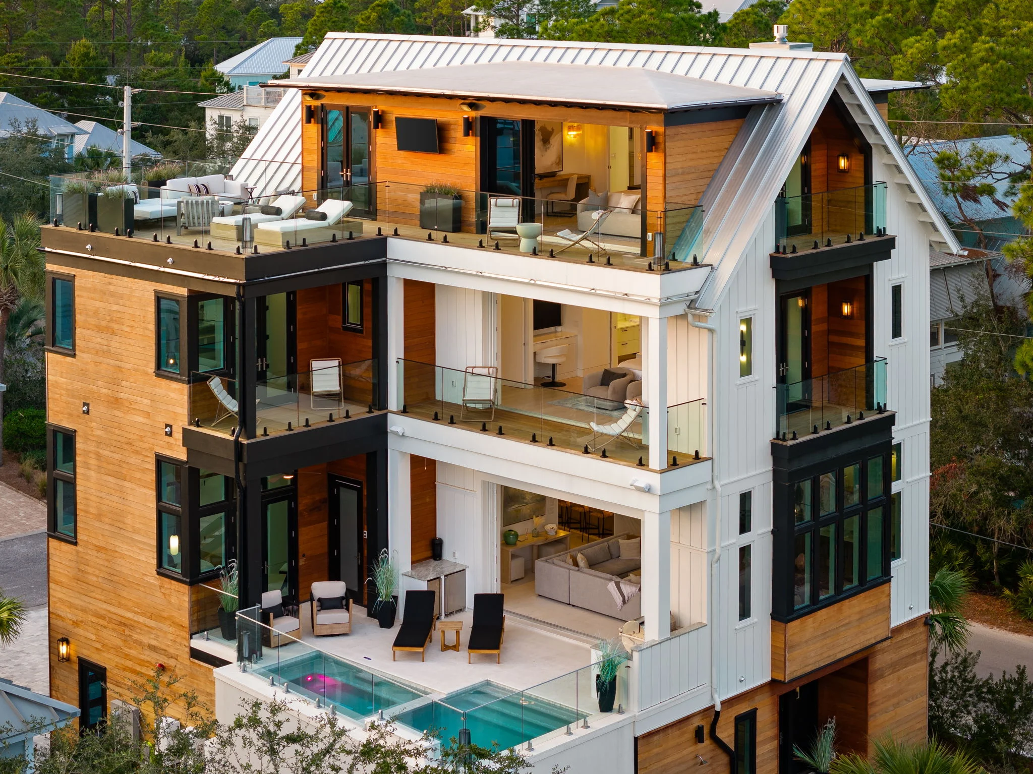 Aerial view of three-story coastal home with glass balcony railings and pool terrace below