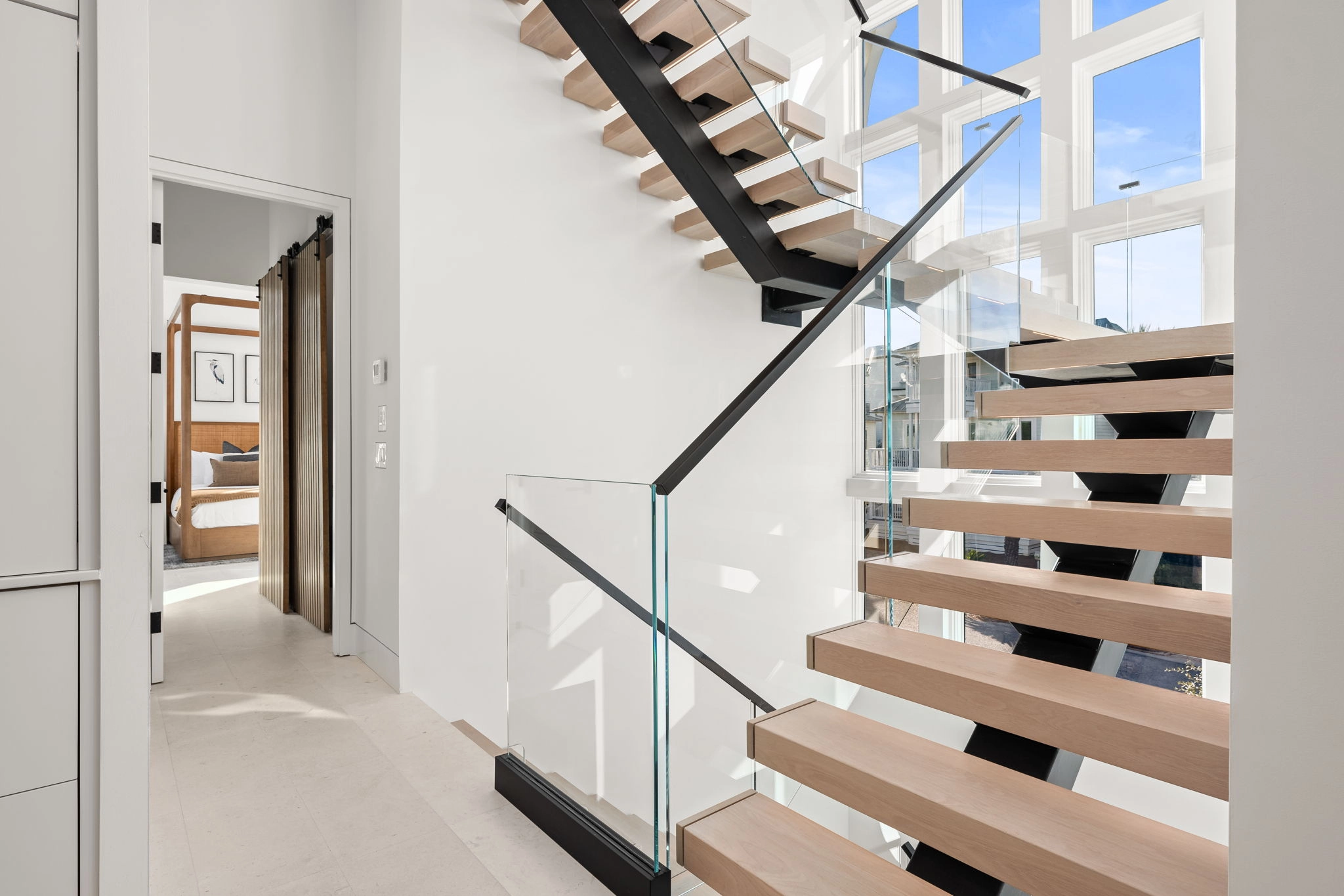Lower flight seen from the hall, glass panels and black handrail against white walls
