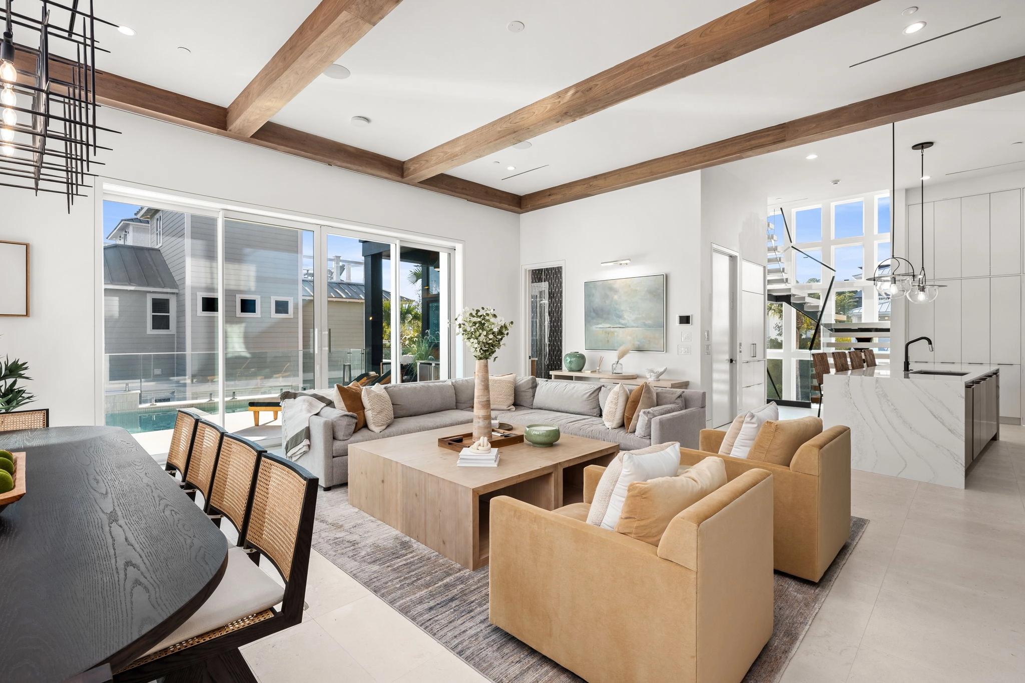 Open living room with wood ceiling beams and sliding doors onto the pool deck