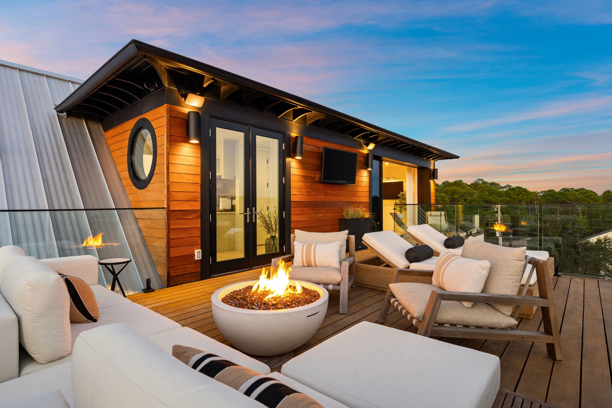 Rooftop lounge at sunset with fire pit, seating and glass railing at the edge