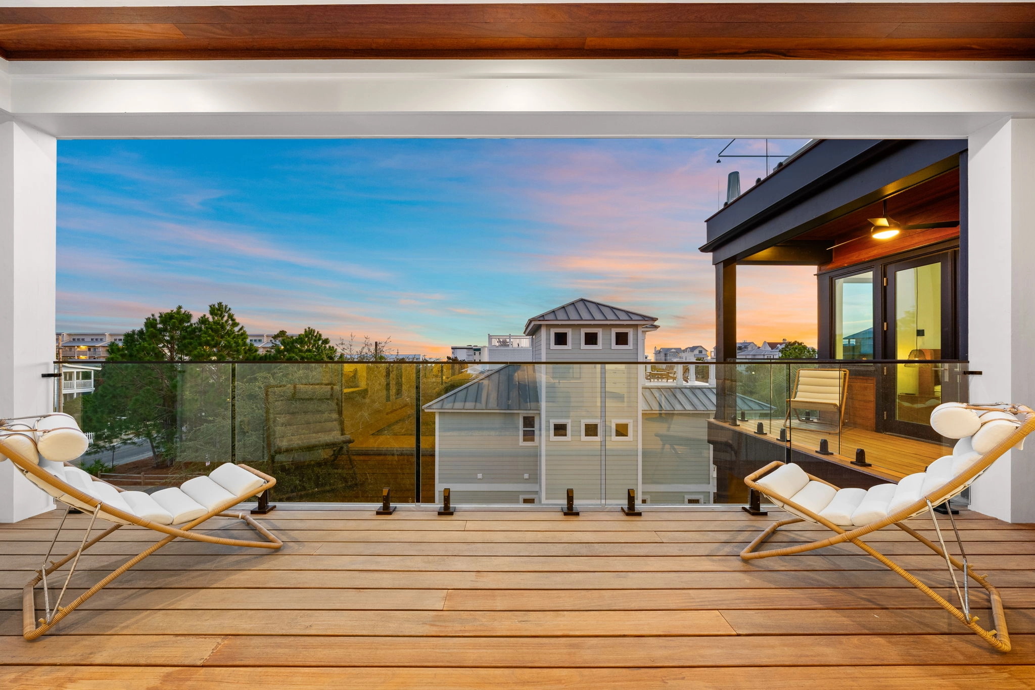 Wood deck flanked by loungers with glass railing opening to neighboring rooftops