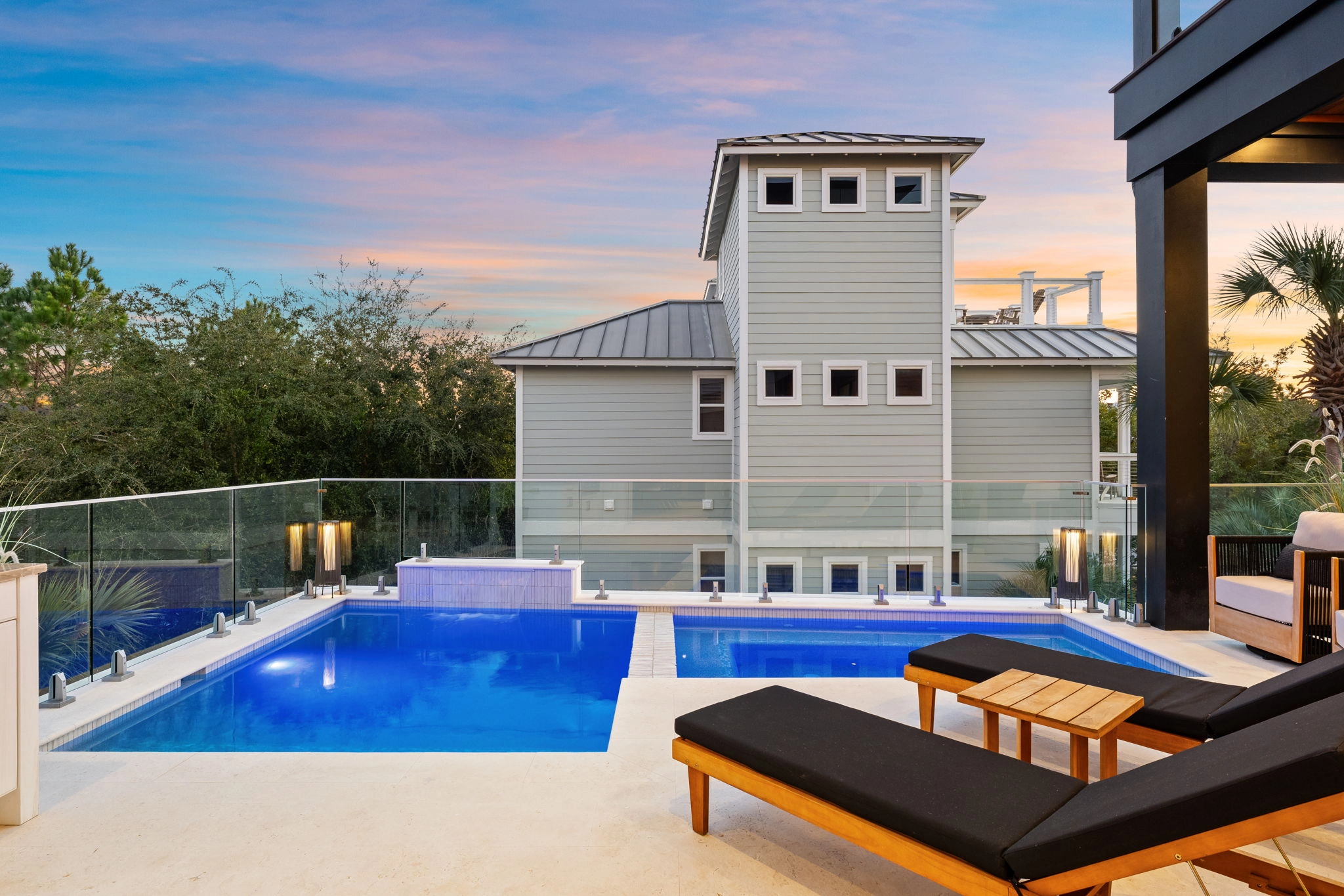 Pool terrace at dusk with glass railing along the edge facing the house