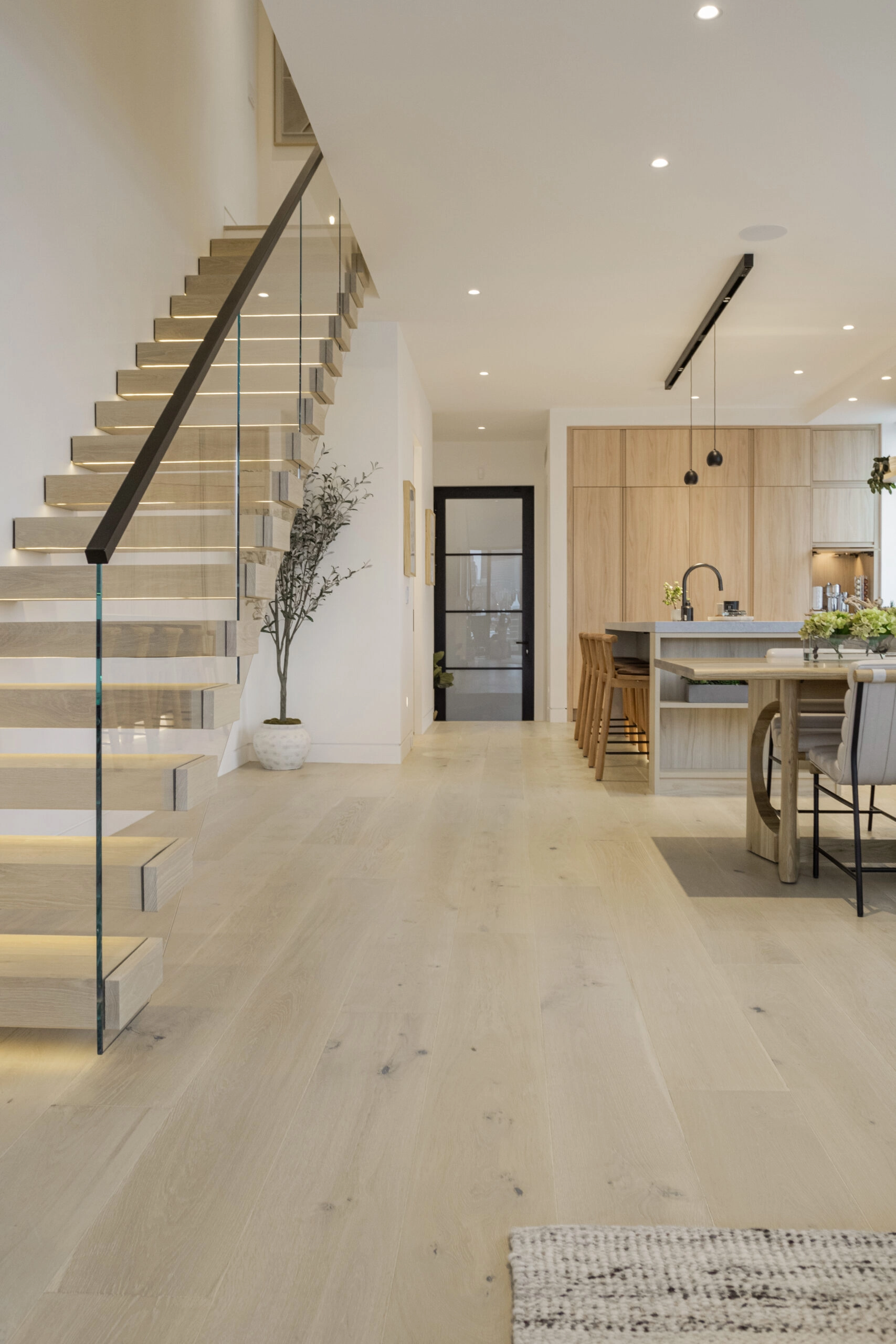 Hall view of cantilevered treads with glass railing and black handrail beside wide-plank floor