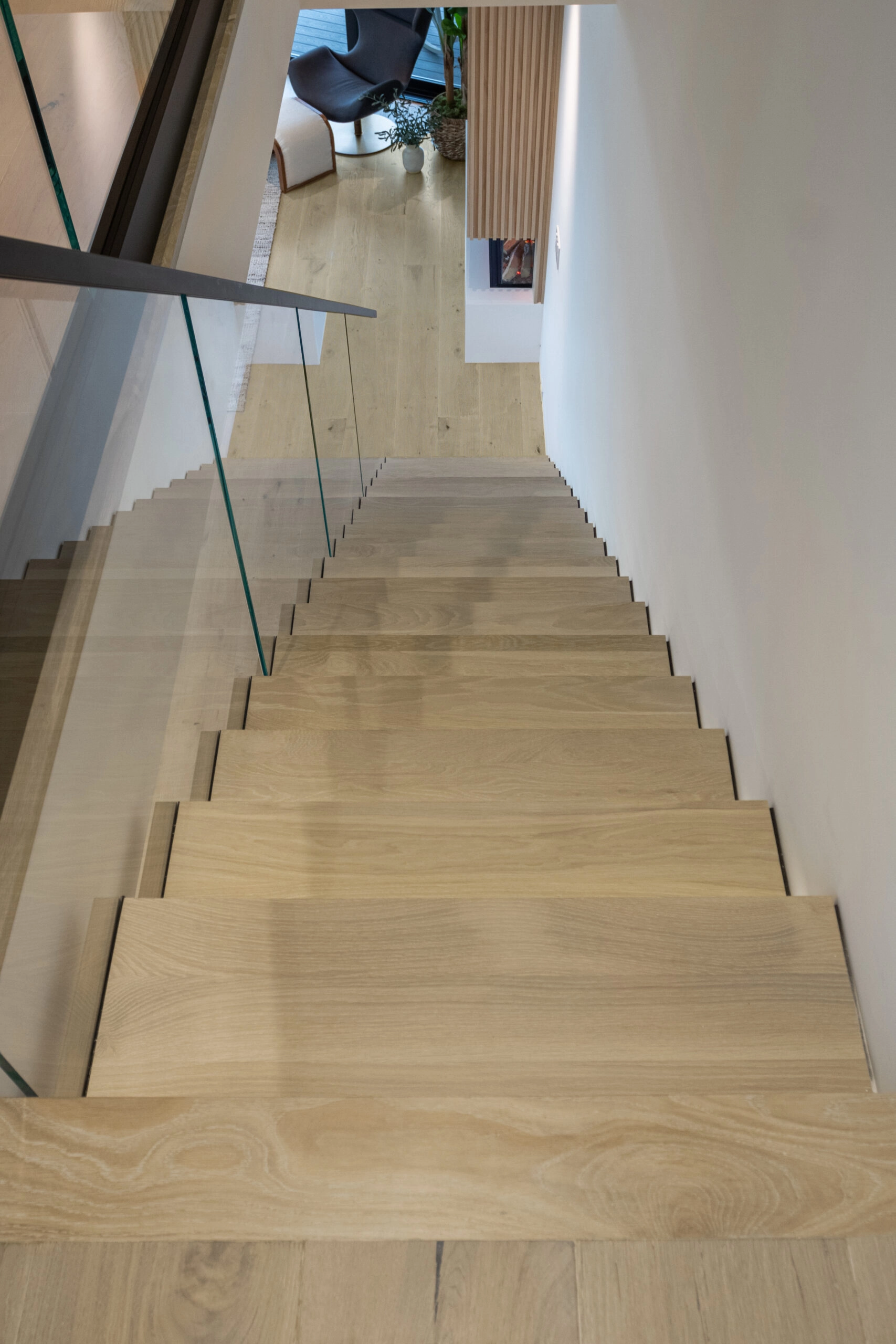 Looking down the flight with glass railing and wood nosings toward the level below