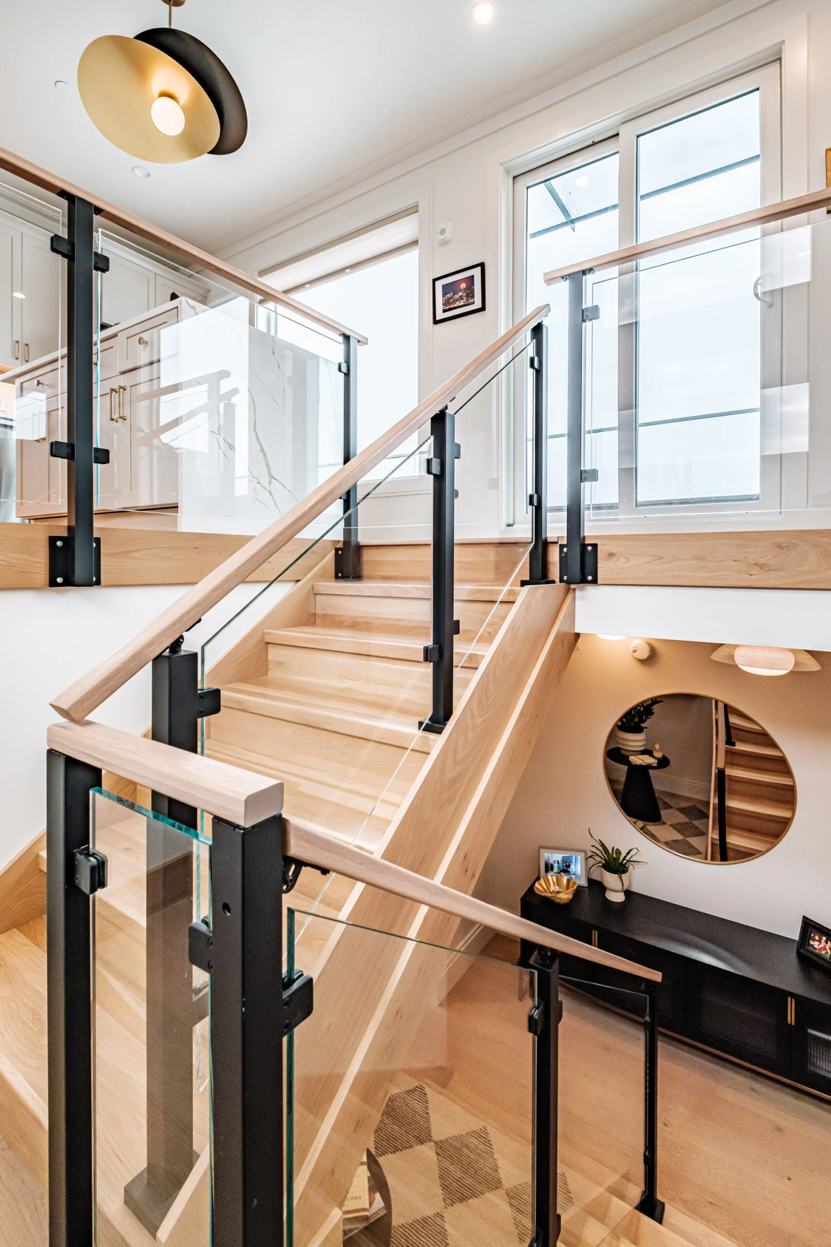 Stairwell from above with glass panels between black posts and a wood top rail