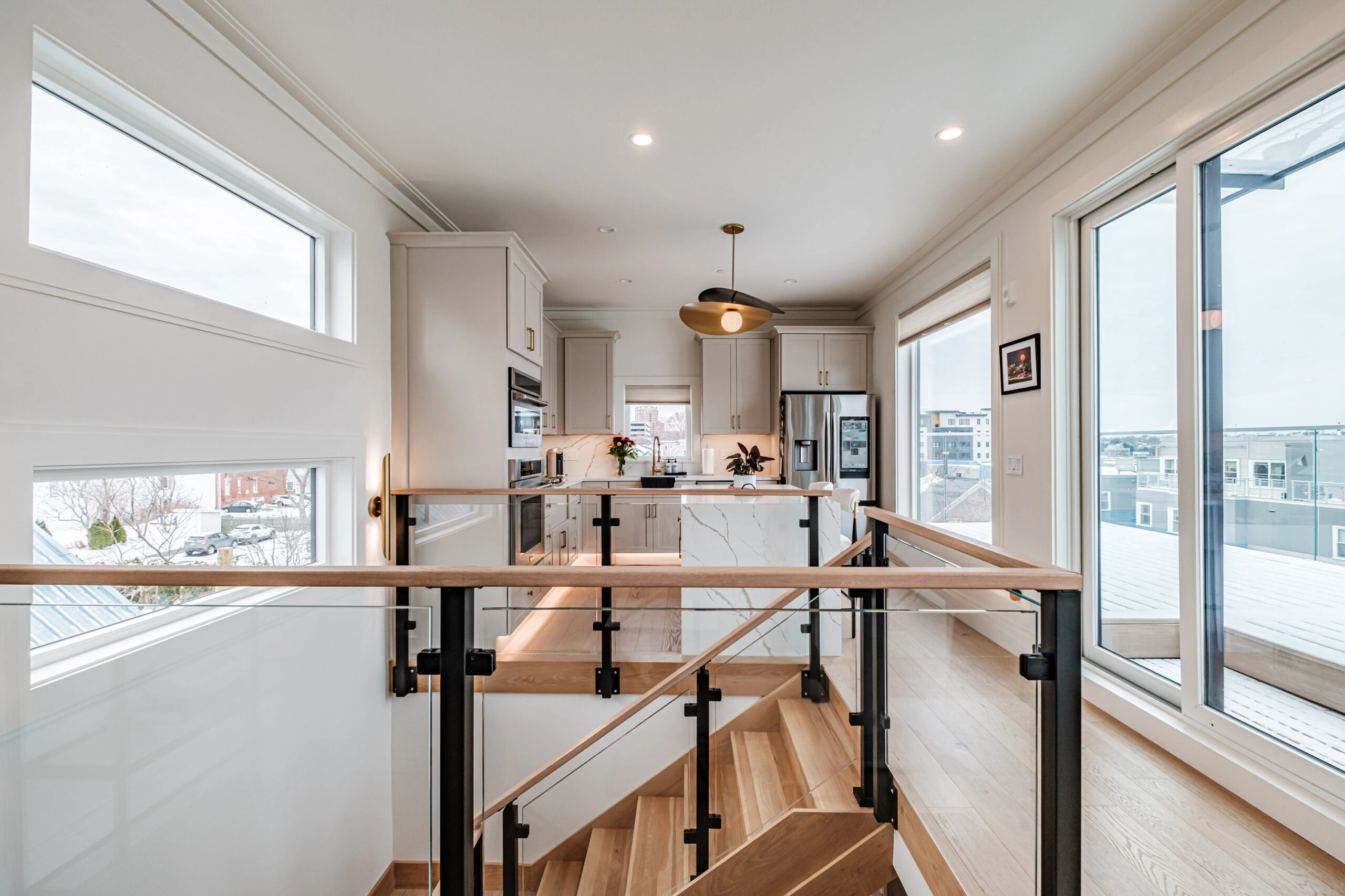 Kitchen seen across the stair opening, railing posts framing the wide-plank floor