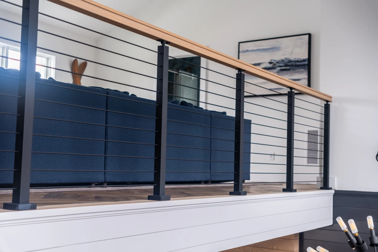 Rod railing along an overlook with wood top rail and blue sofa beyond