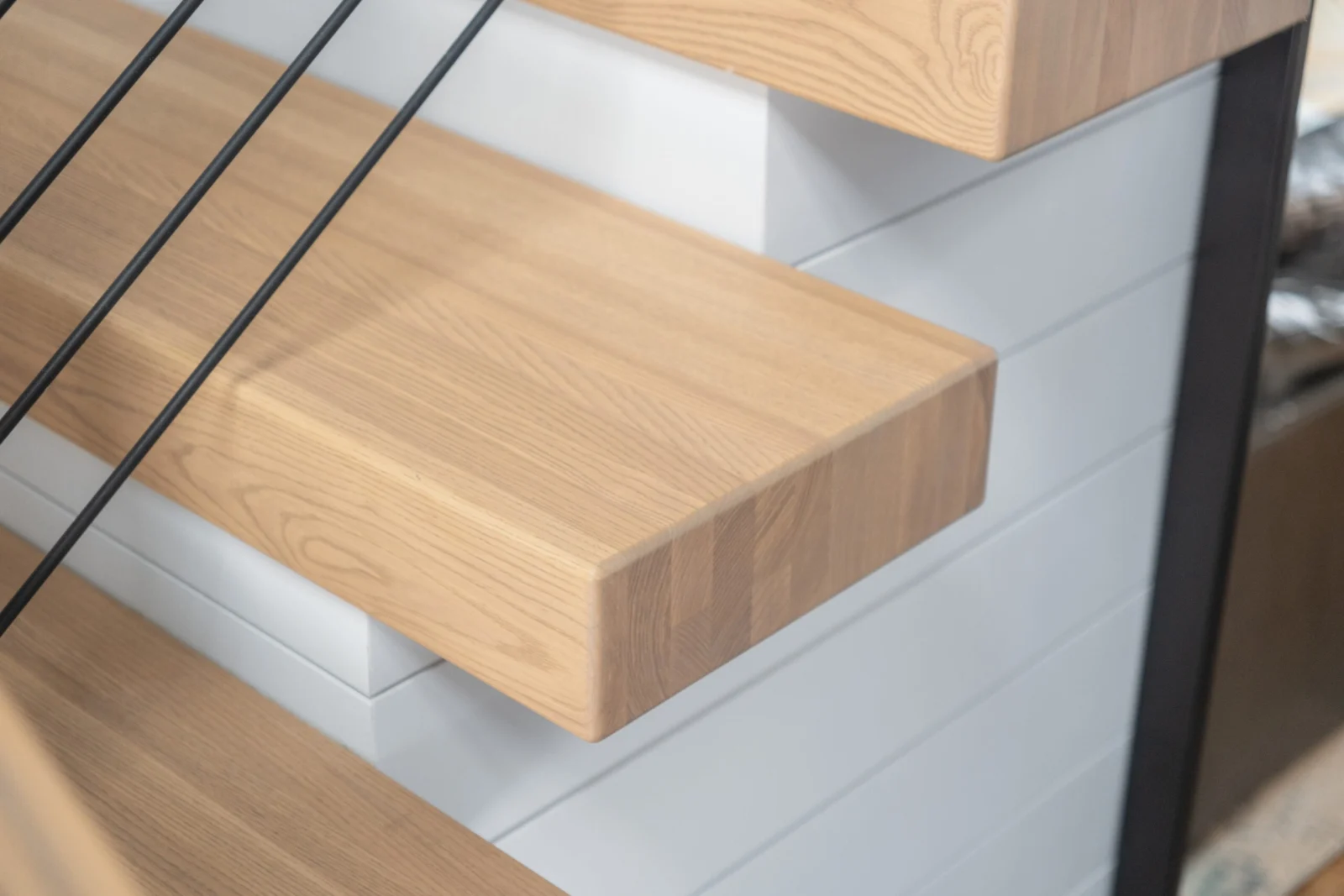 Close view of two cantilevered treads meeting a black stringer and shiplap wall