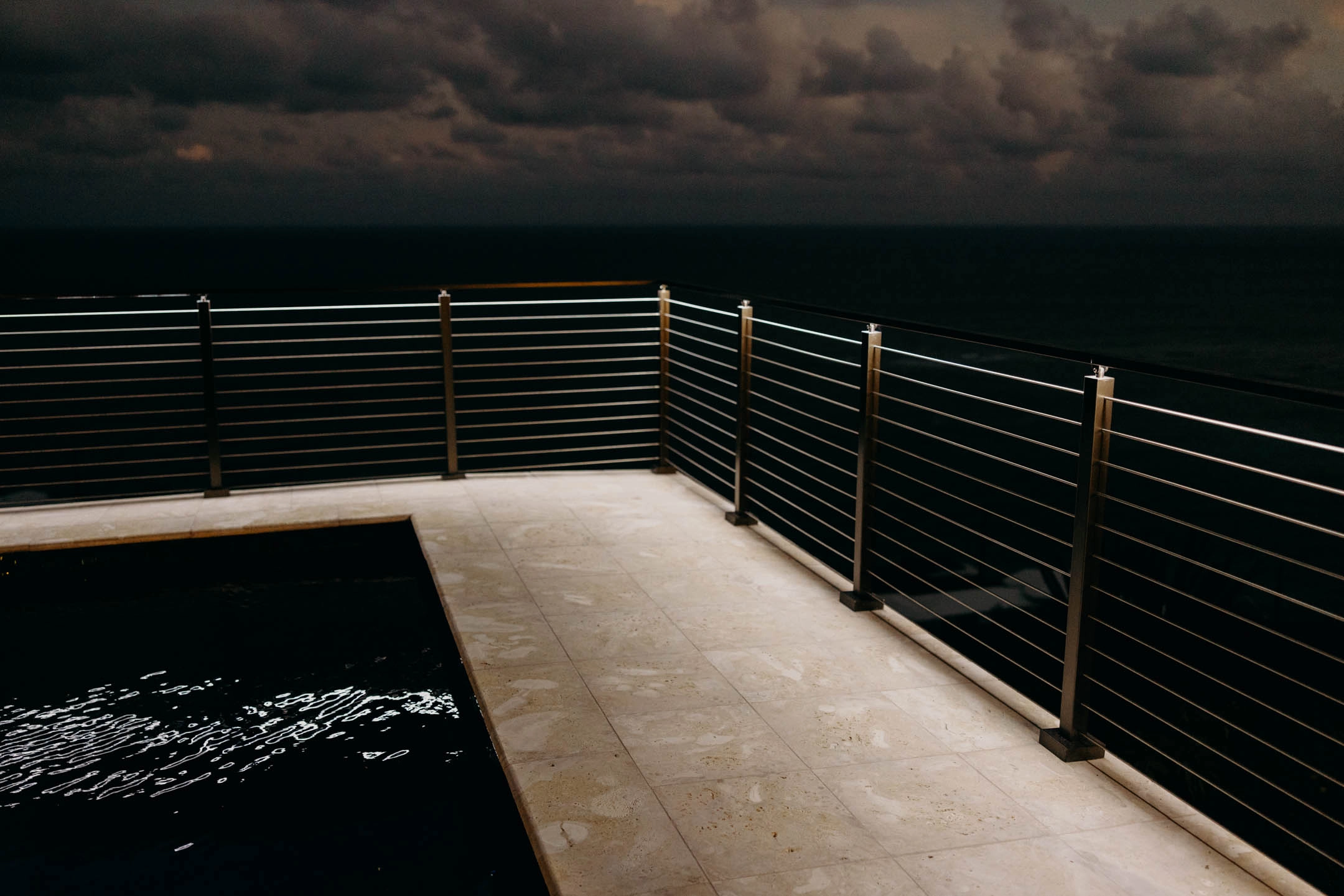 Railing with integrated handrail LEDs wraps around a pool overlooking the ocean at night