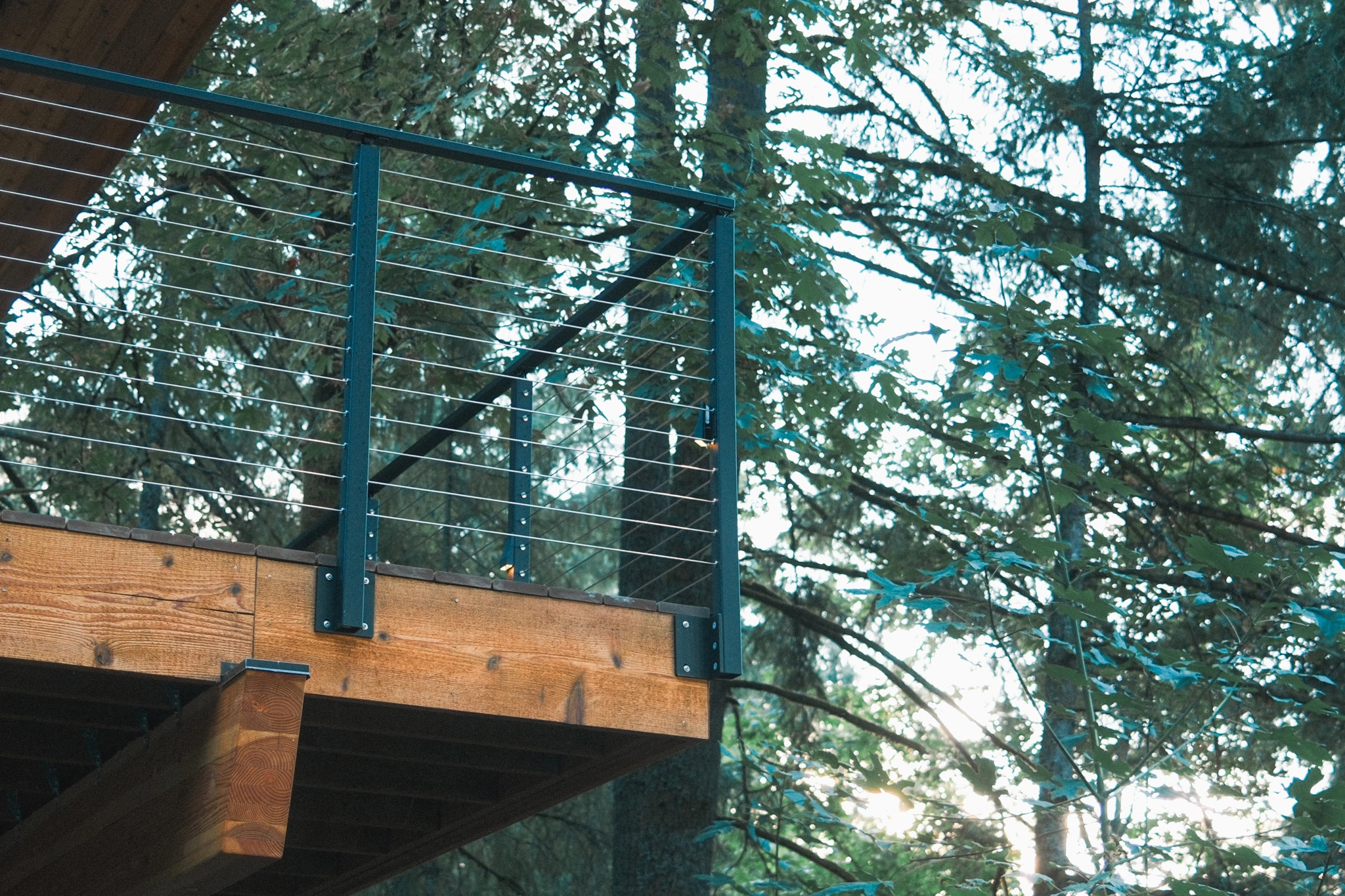 Side-mounted posts bolted to a beam carrying cables at a deck corner