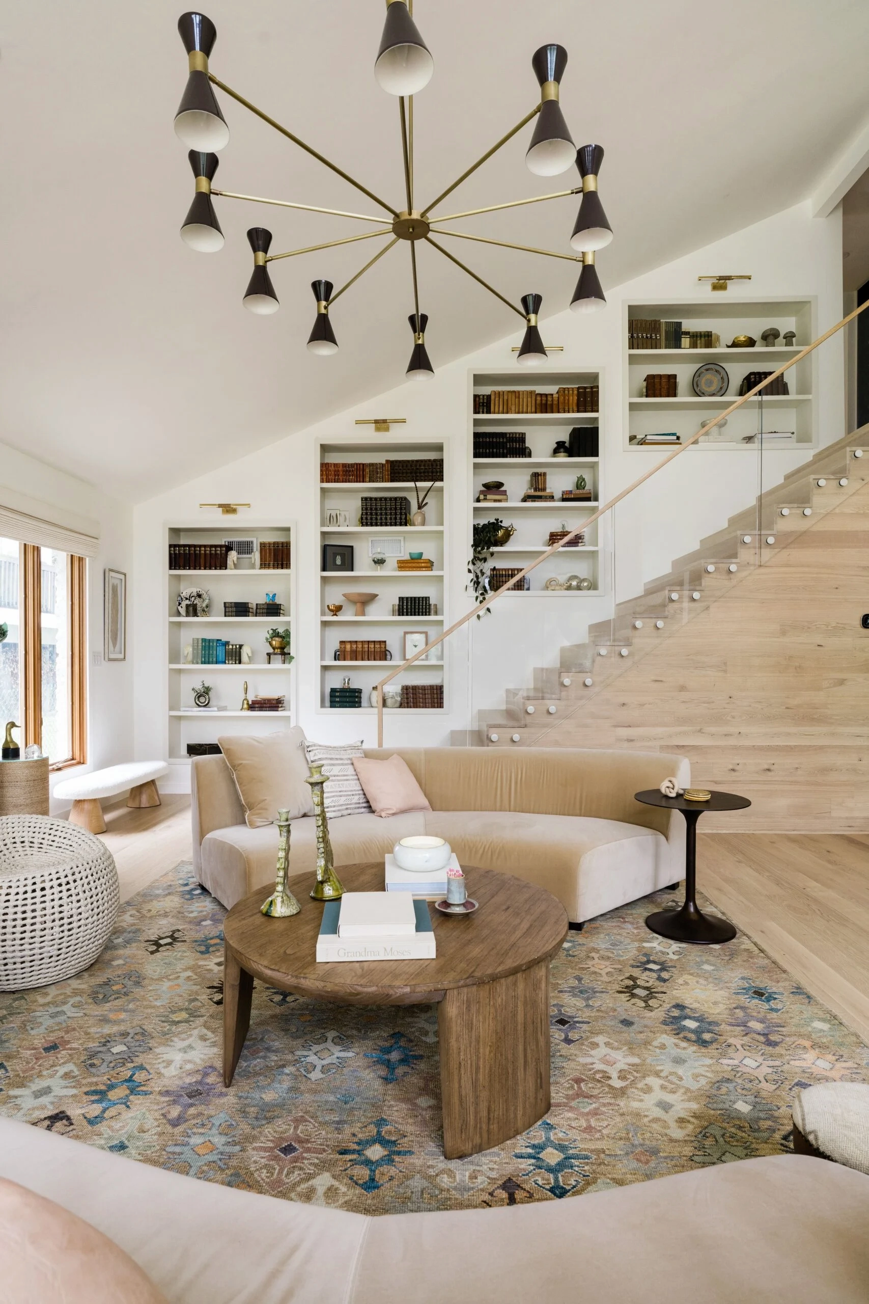 Living room under a vaulted ceiling with a glass-railed stair rising along built-in shelving