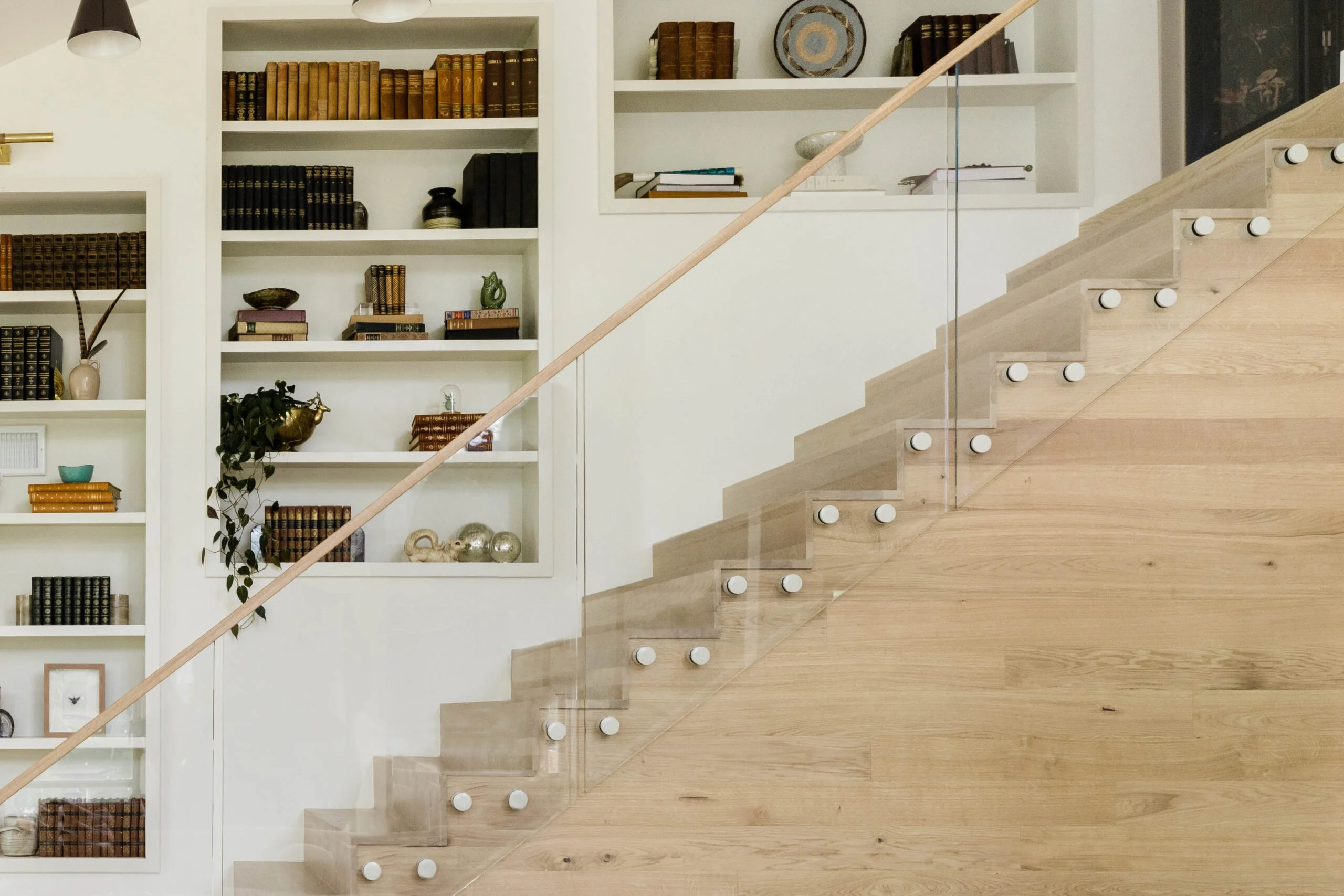 Stair flight with glass panels held by round metal pins and a slim wood handrail