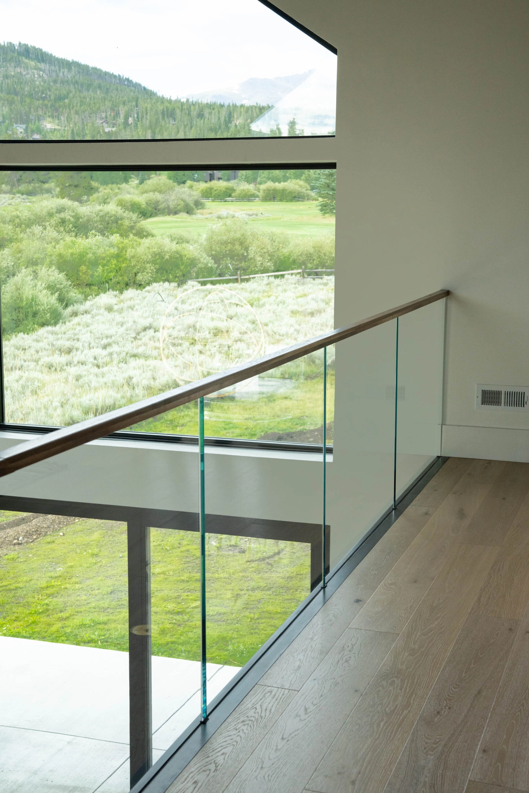 Upstairs walkway with glass railing and wood top rail beside a wide mountain-view window