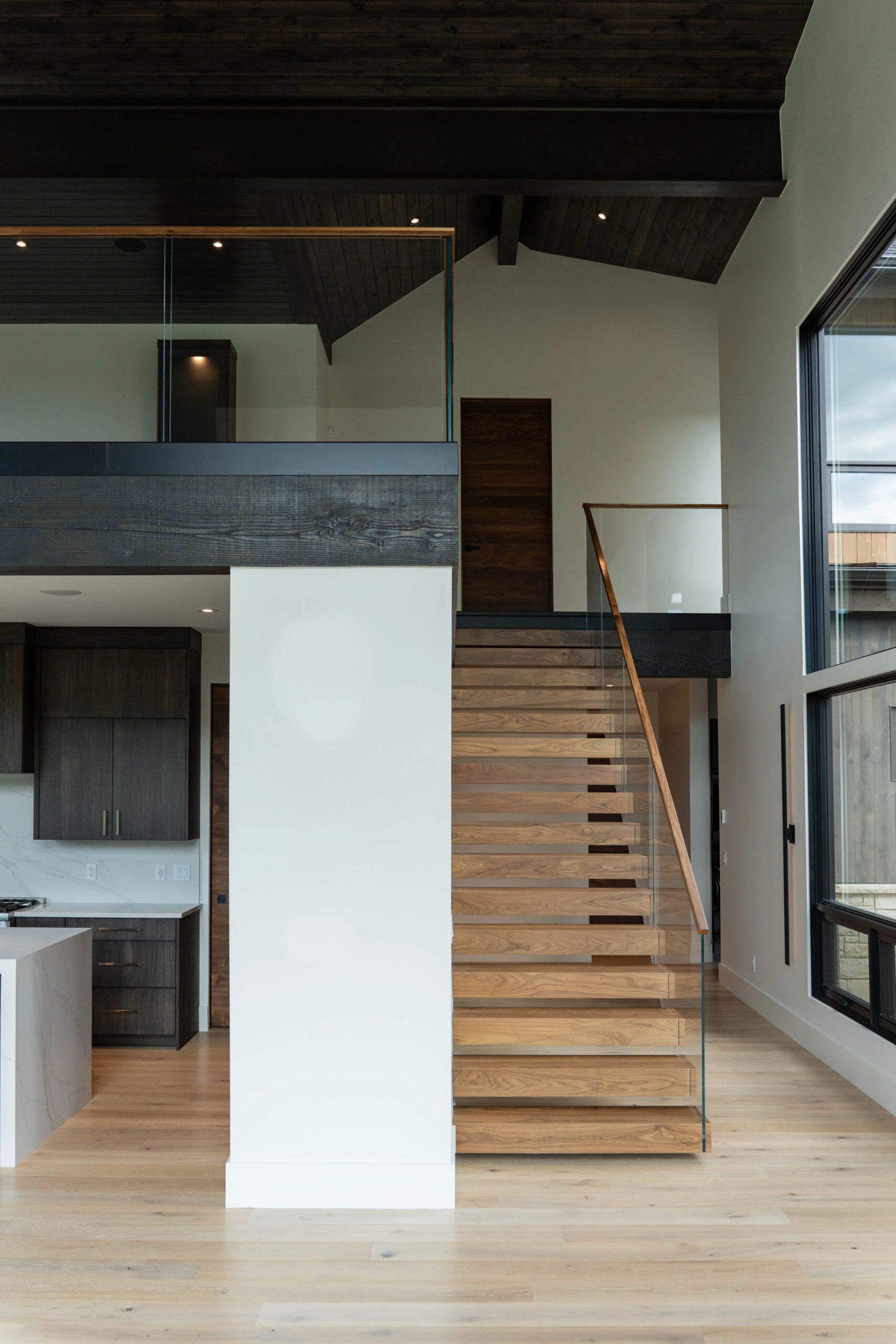 Wide interior view of a stair with glass railing rising past a vaulted plank ceiling
