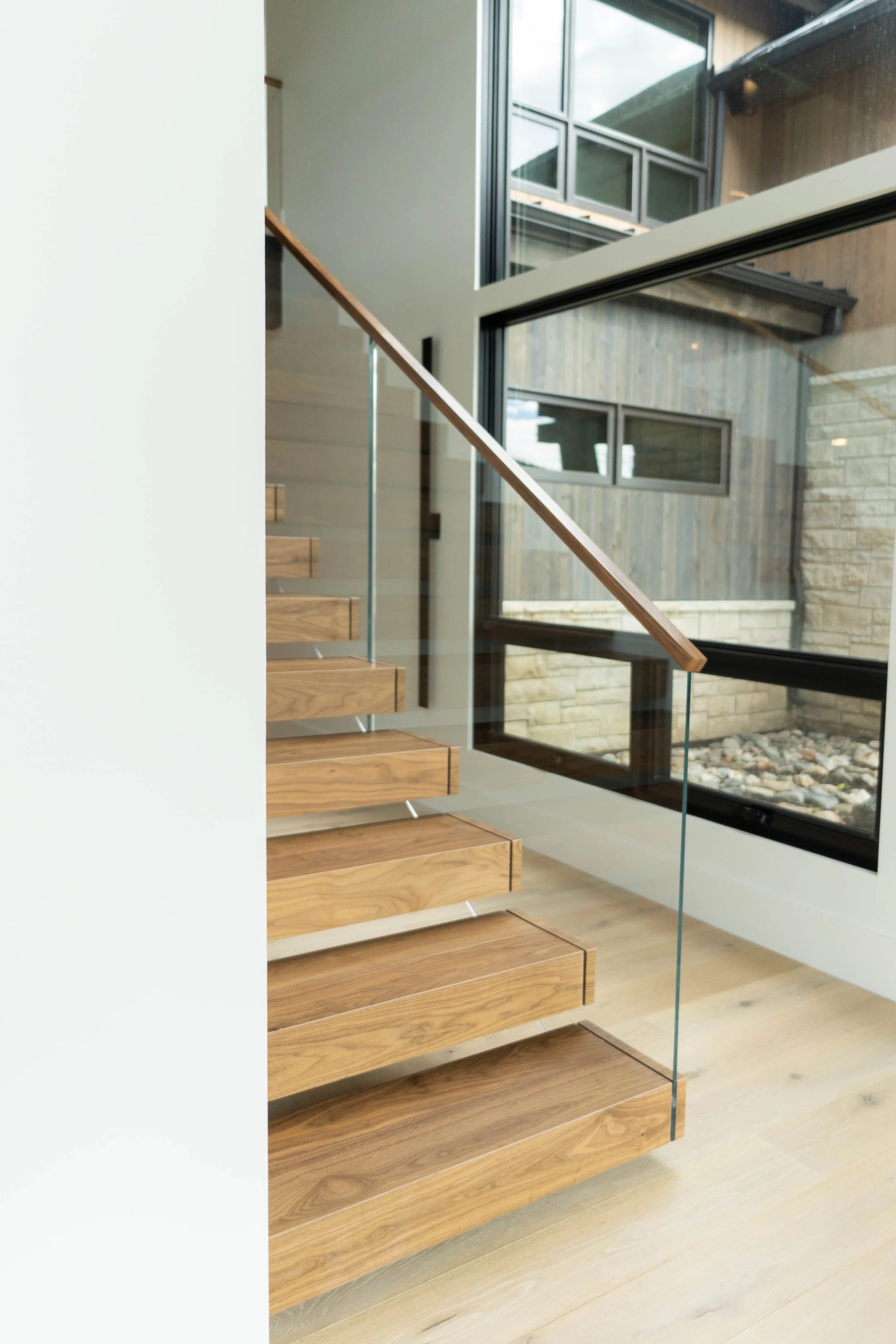 Wood treads and glass railing with a linear fireplace and stone wall beyond
