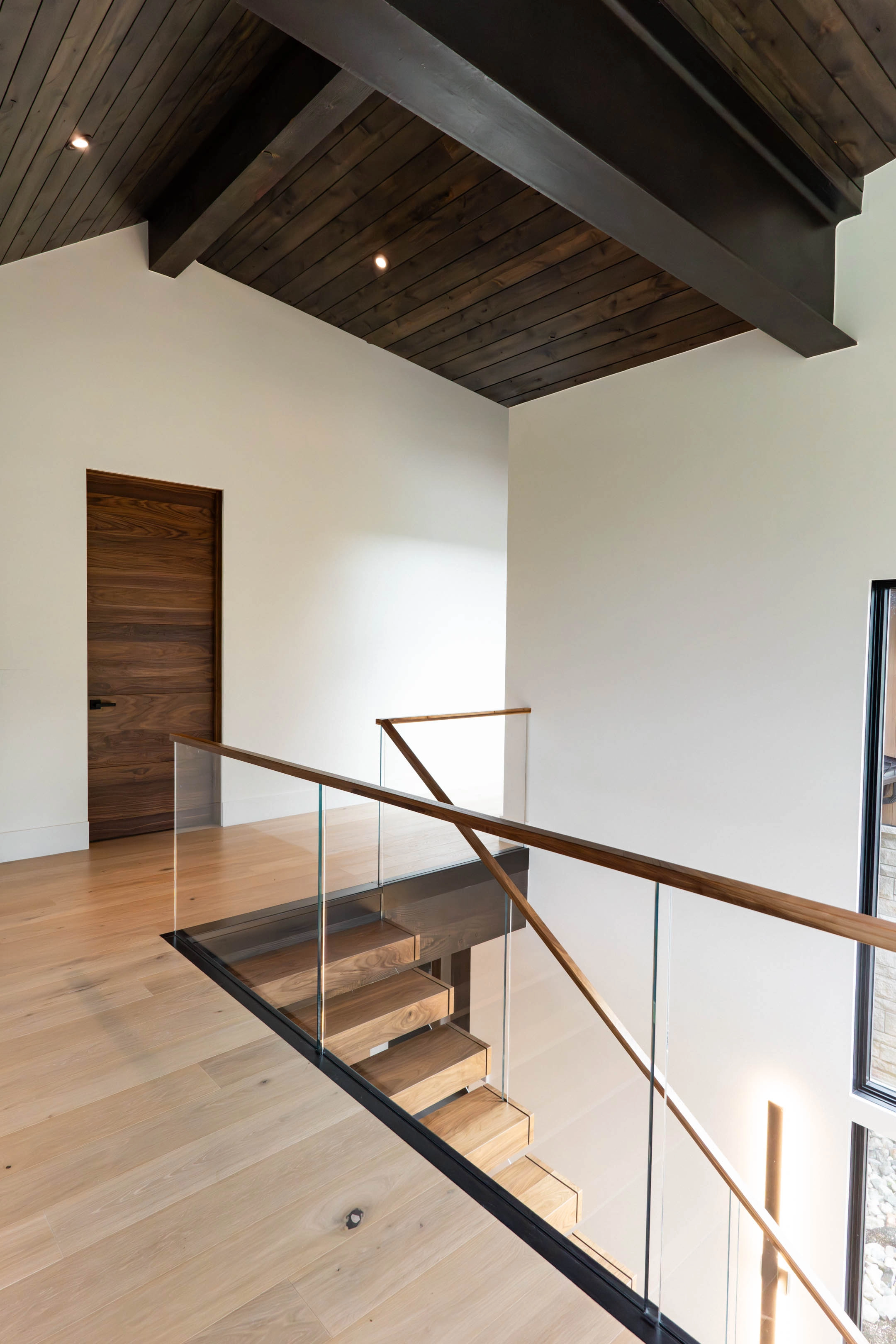 Upper hall with glass railing wrapping the stair opening under exposed dark beams