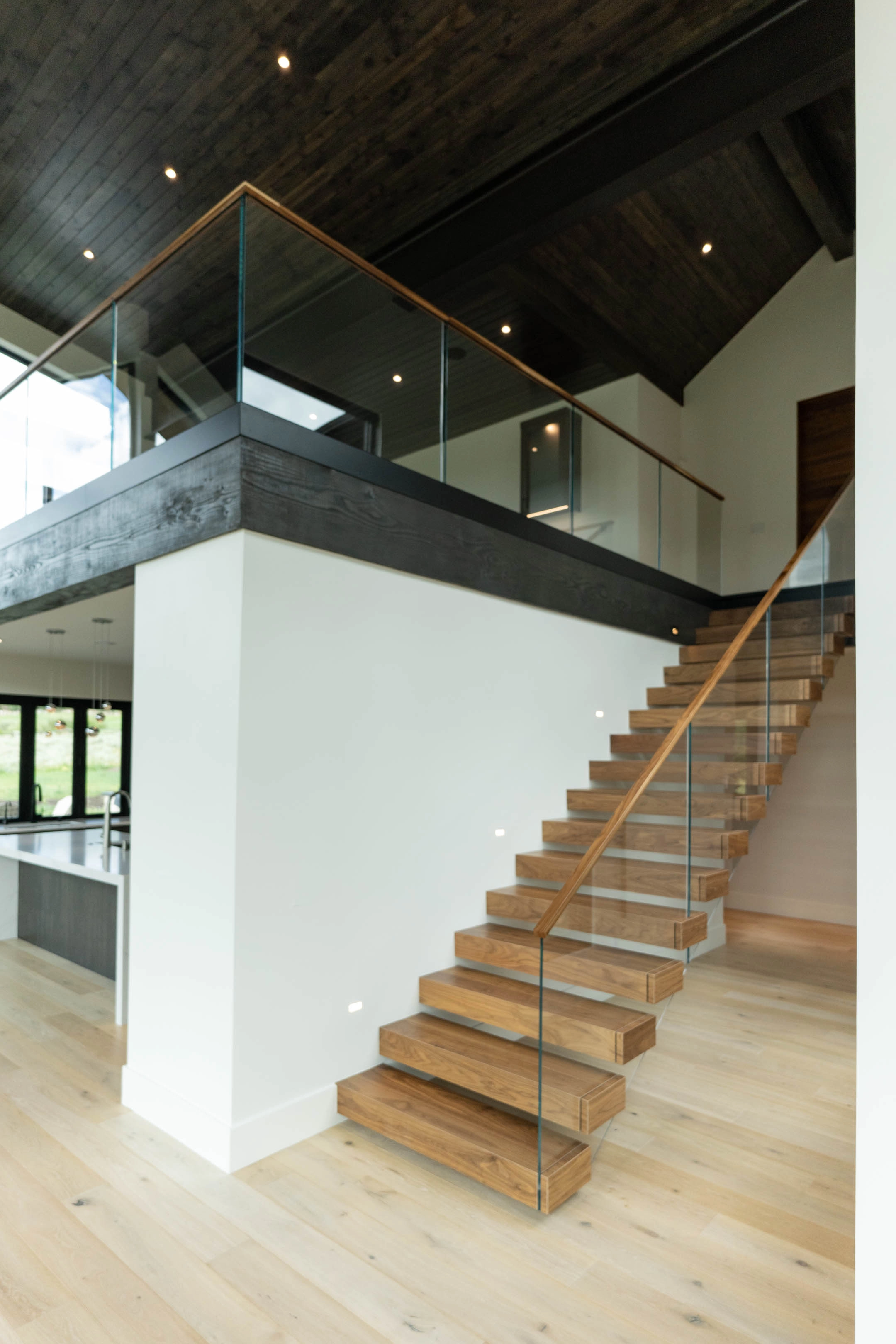 Full stair run with glass railing climbing to a loft guarded by more glass