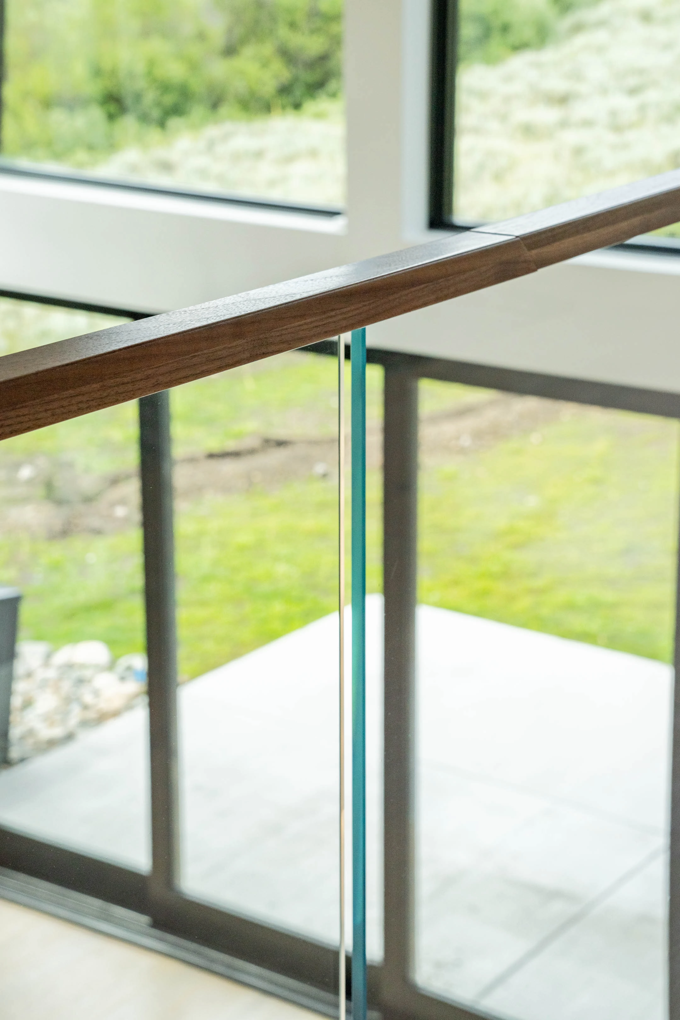 Detail of a wood cap rail meeting clear glass panels above a patio view