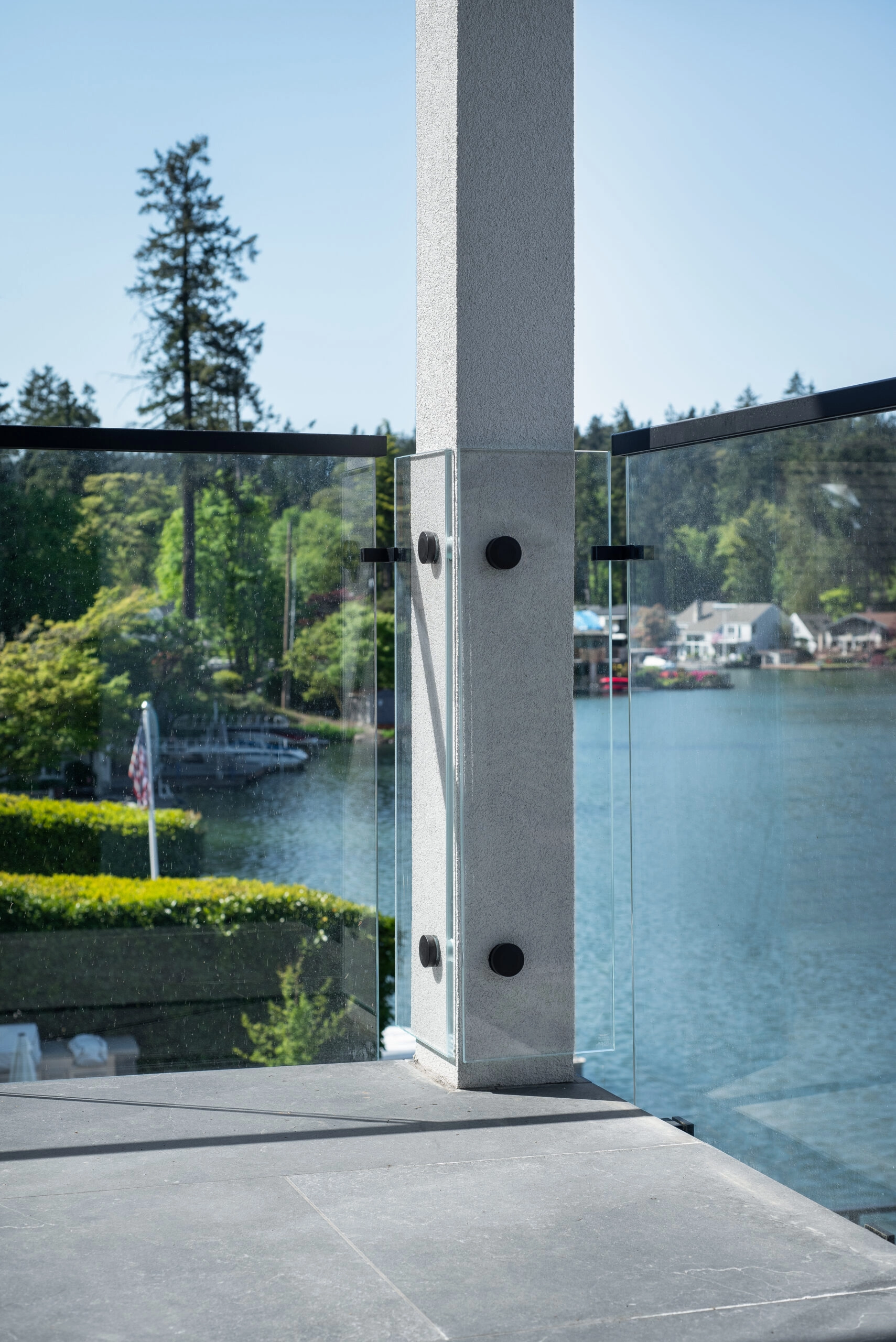 Glass panels meeting at a column on black clamps with the lake beyond
