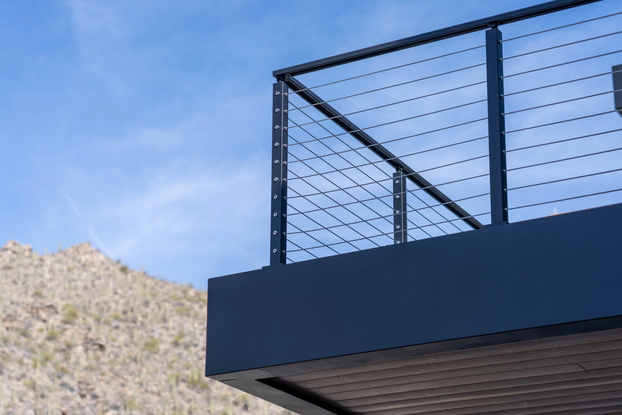 Black cable railing on a cantilevered balcony seen against a desert hillside