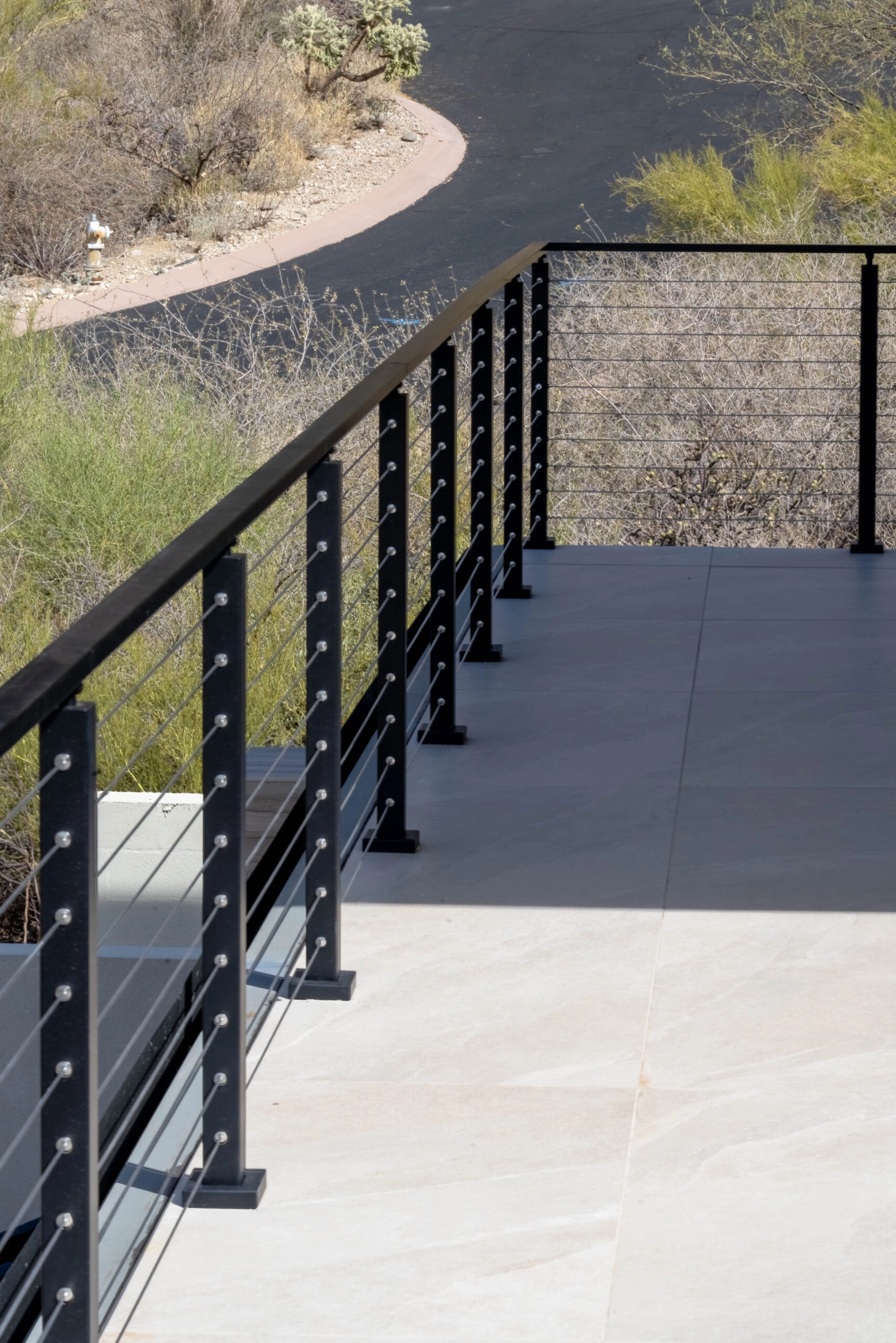 Cable railing edging a concrete patio above a curving desert driveway