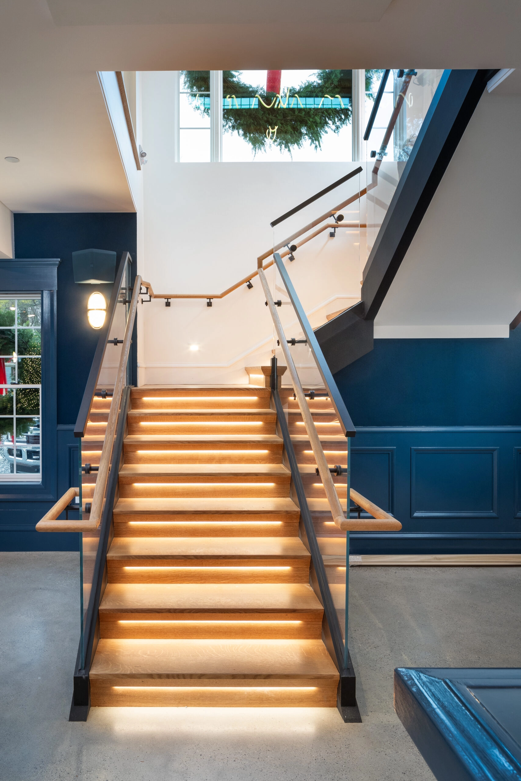 Straight view up a glass-railed stair with wood handrails on both sides