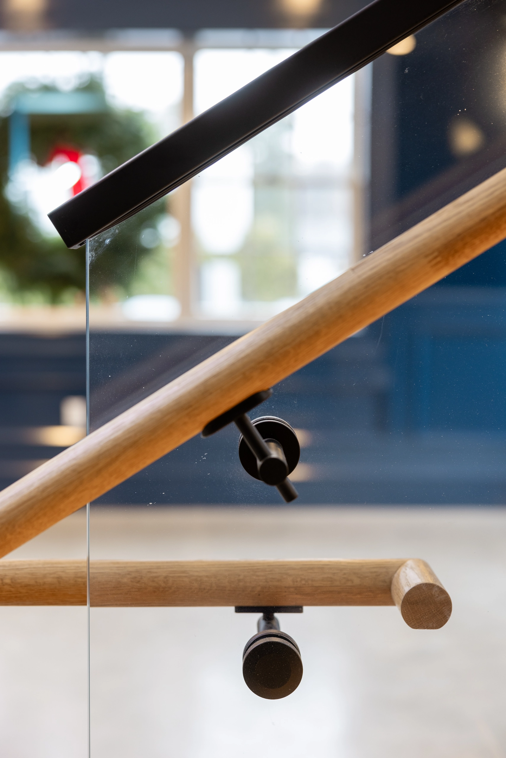 Wood handrail clamped through a glass panel below a black top rail