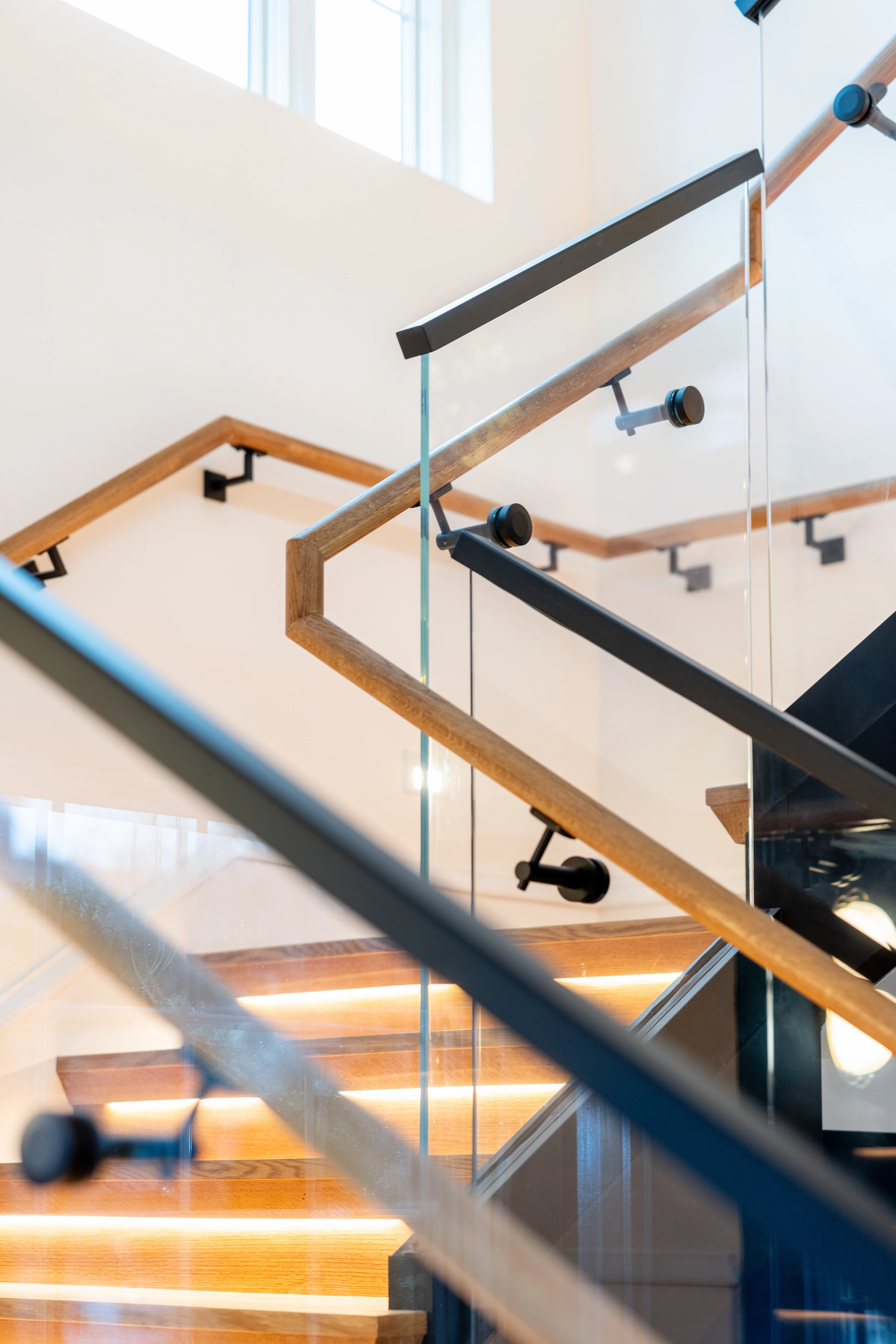 Wood handrails turning against white walls above a glass-guarded stair flight