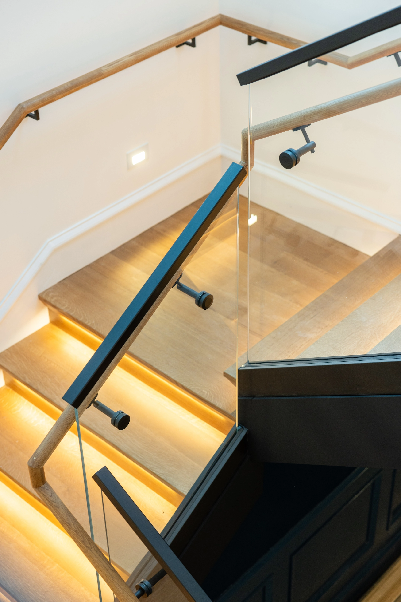 Looking down over glass railing at illuminated treads and handrail returns