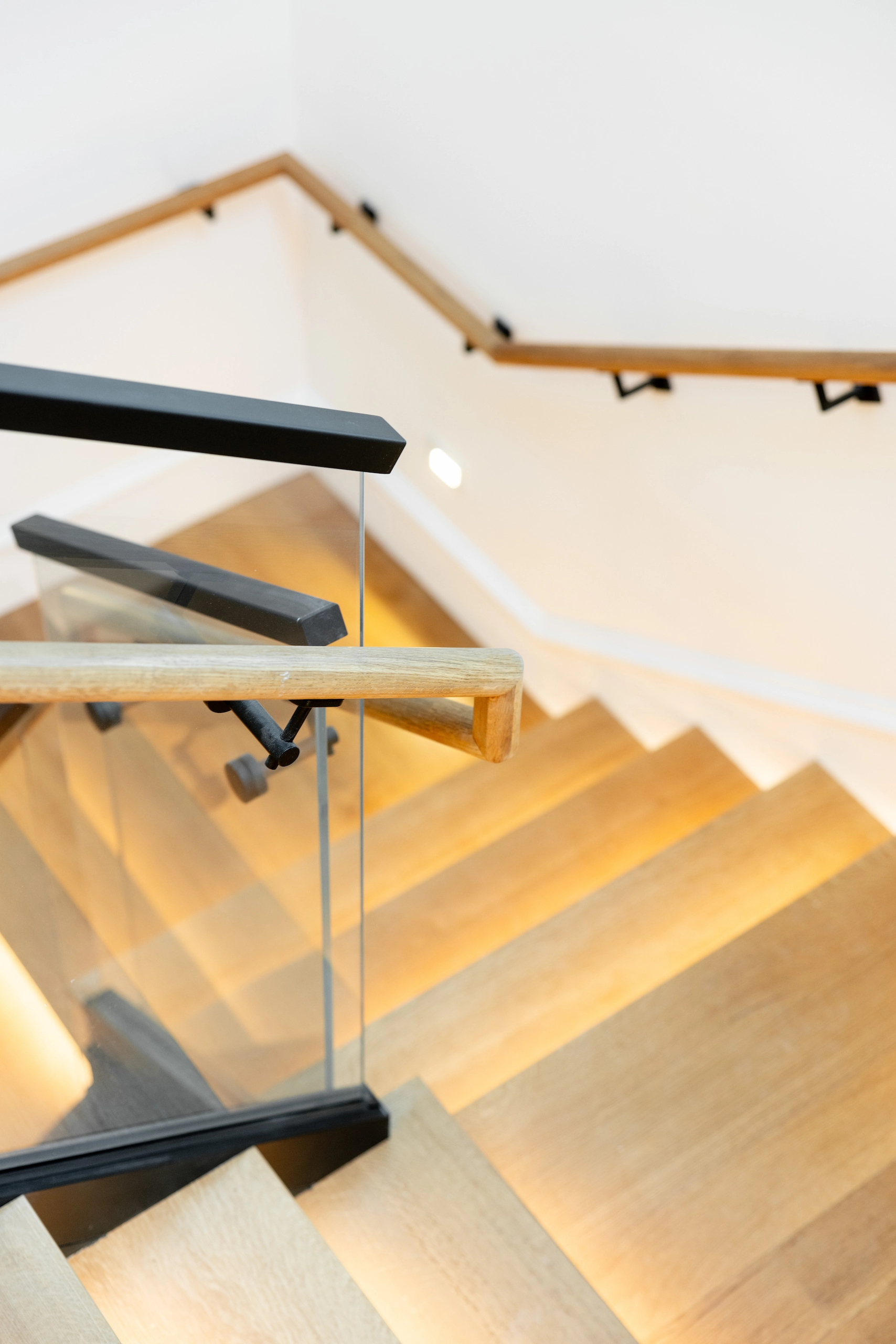 Down a stair flight with a wall-mounted handrail and a single glass panel