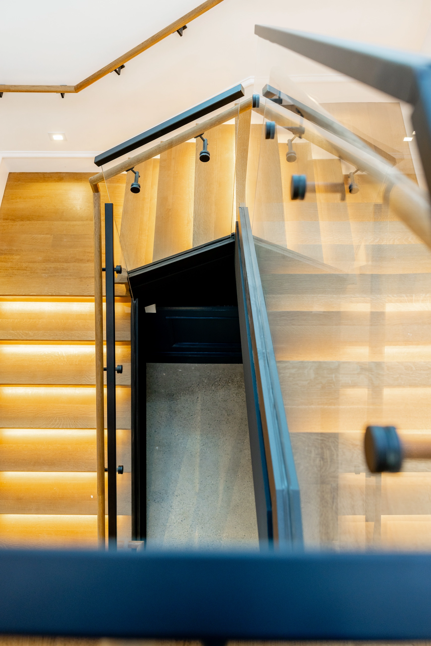 Glass railing beside a lit stair flight dropping into a lower landing