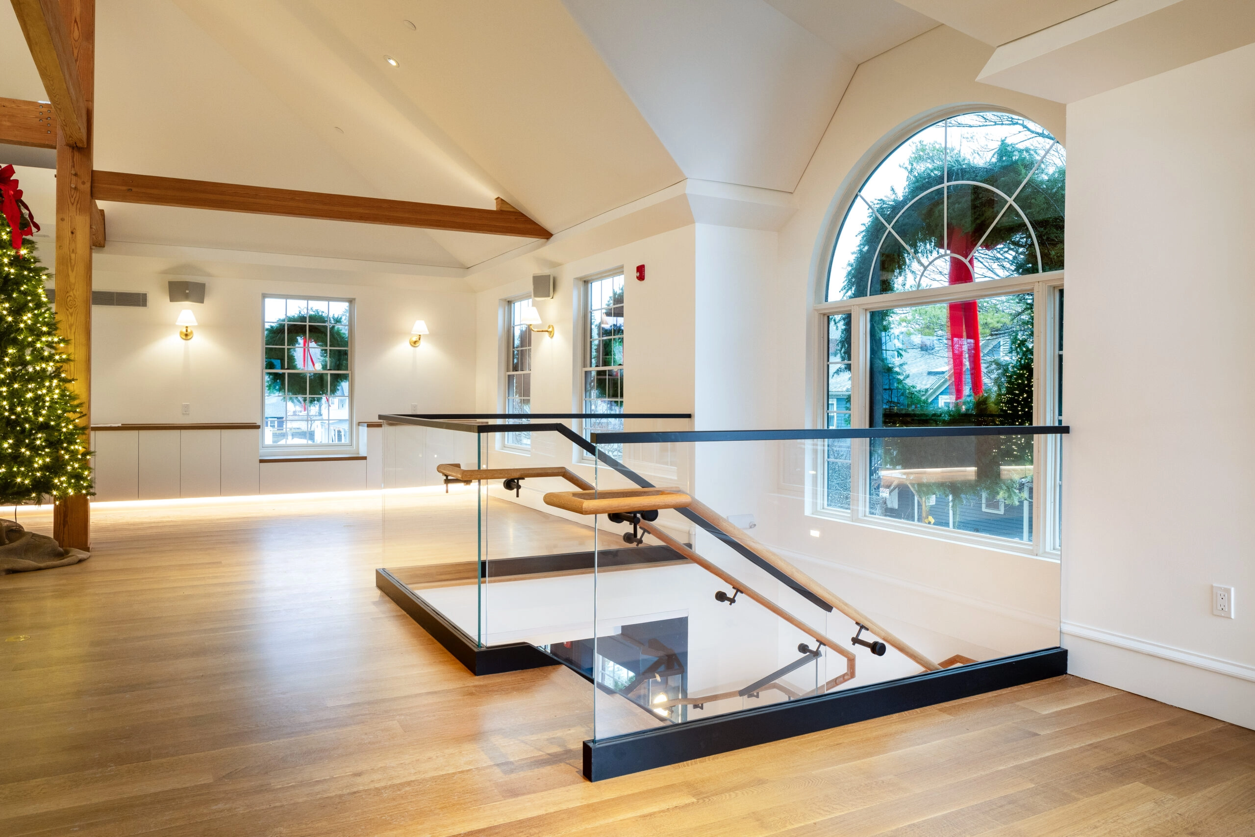 Open room with a glass-guarded stairwell opening beneath an arched window