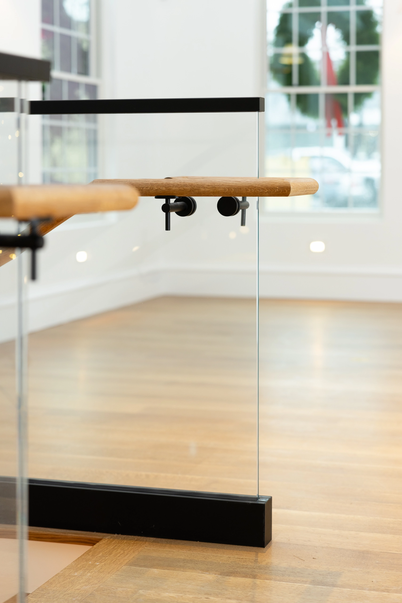 Wood handrail end passing through a glass panel above a black base shoe