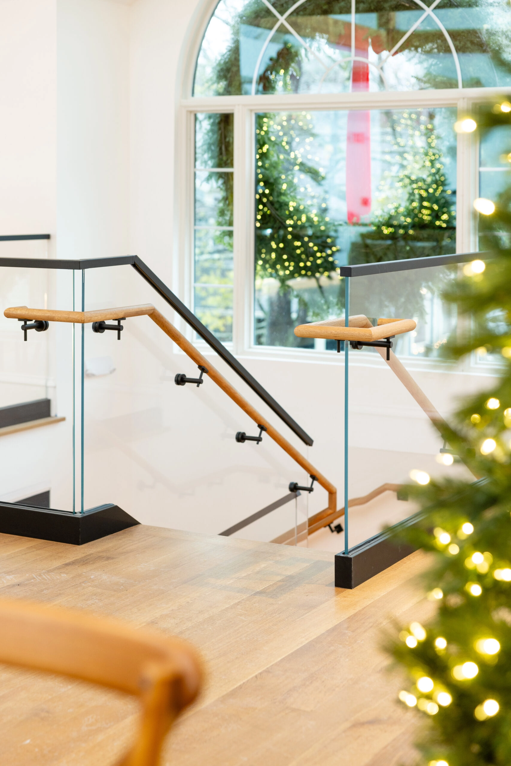 Stair head with black and wood rails beside a window of winter greenery