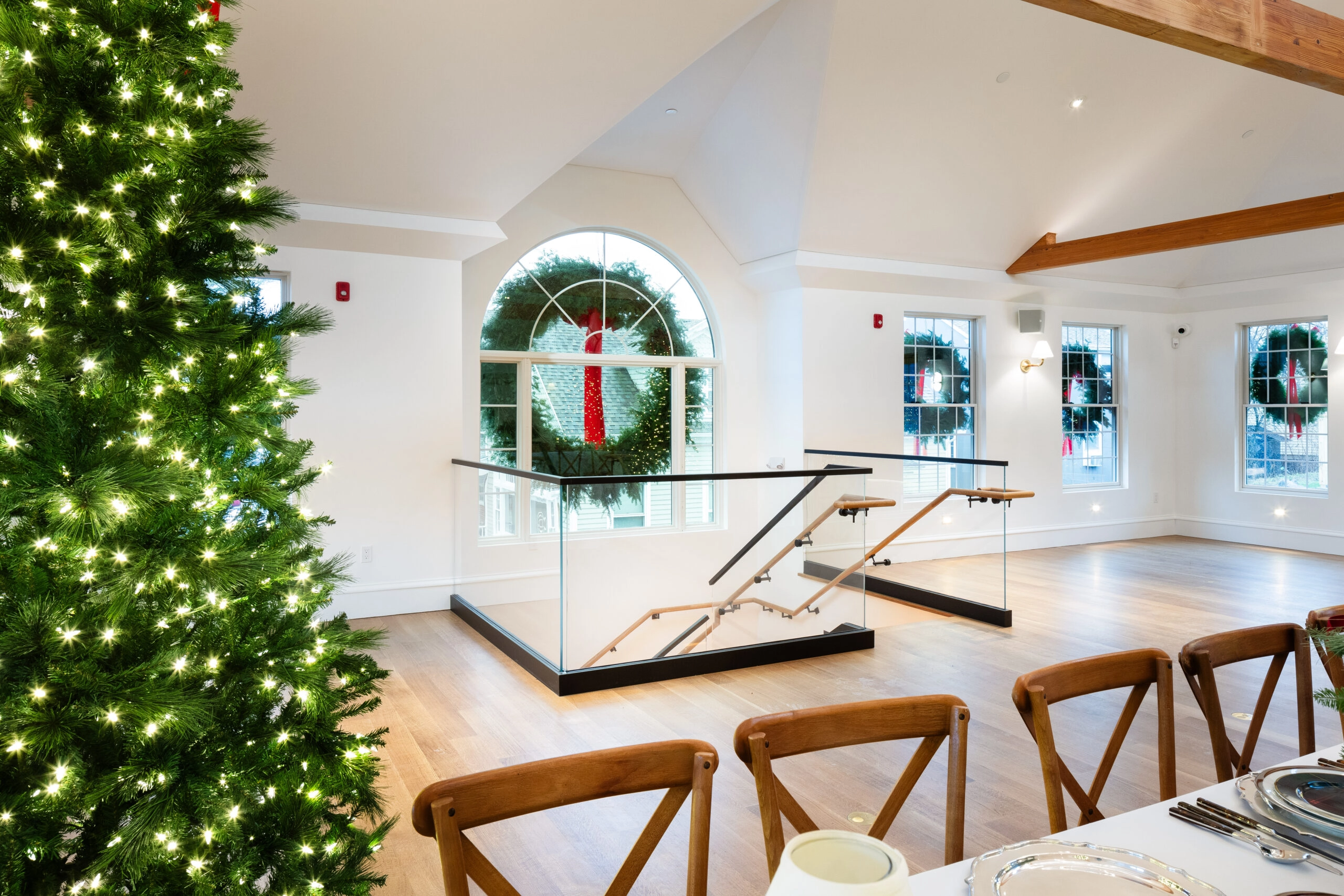 Event room with dining chairs and a glass stair guard near arched windows