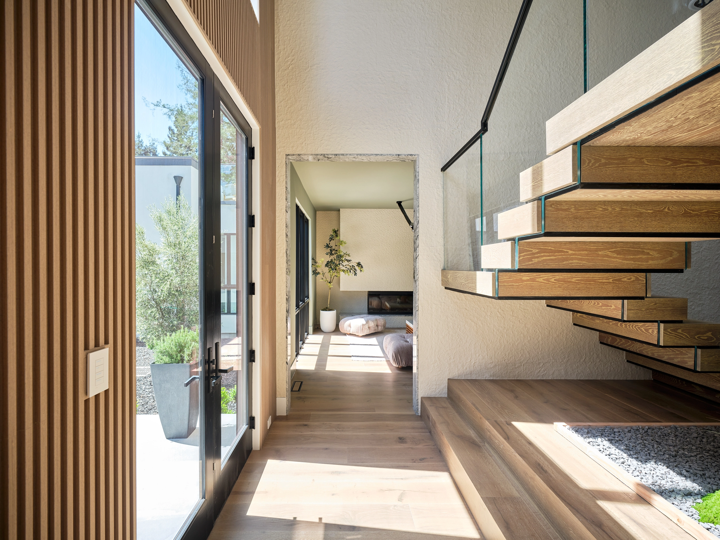 Entry hall with open patio door, stair treads and glass railing rising at right
