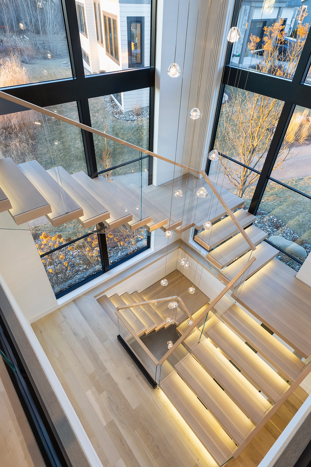 Overhead view down through several levels of glass-railed flights and pendant lights