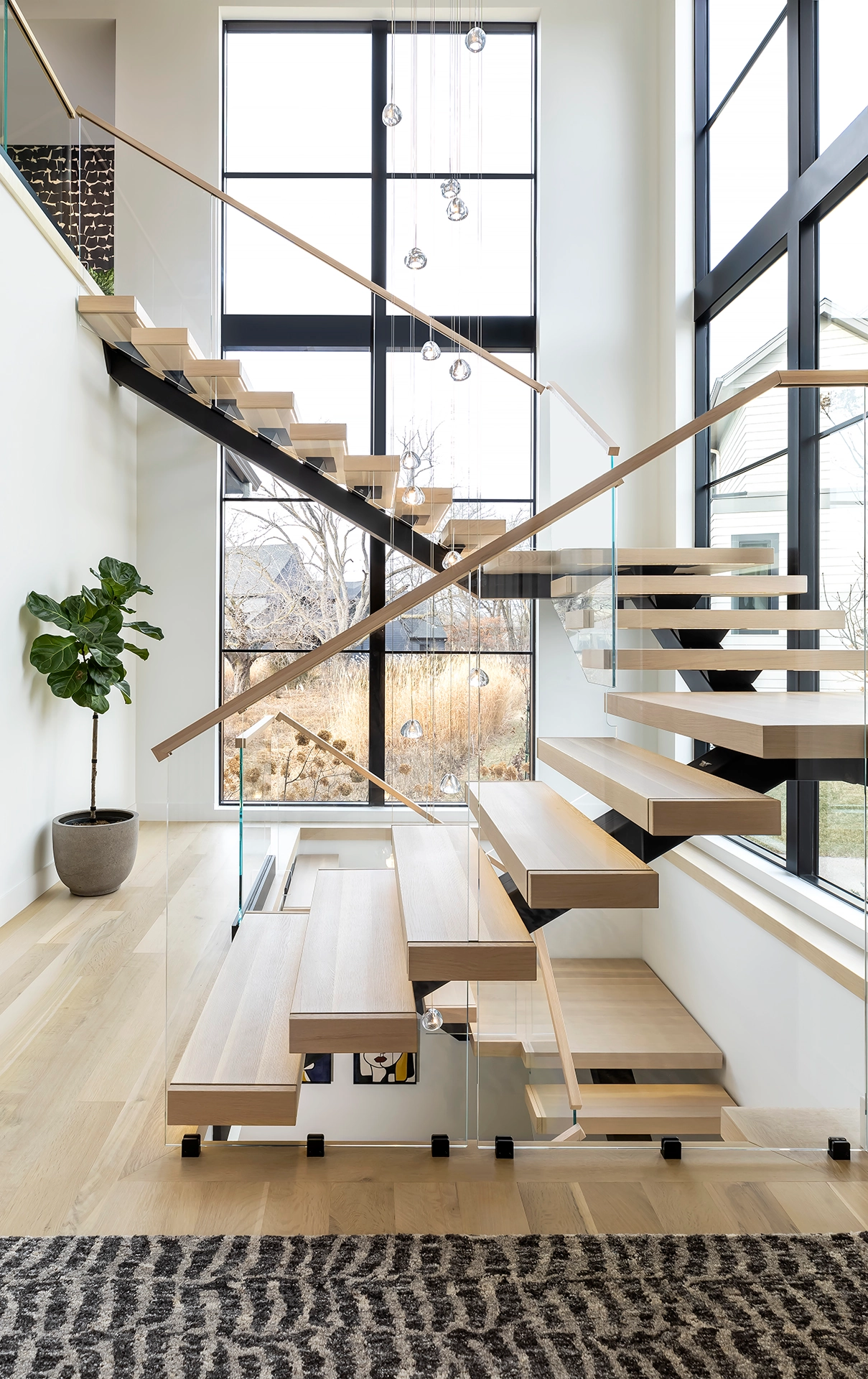 Stacked flights on a black stringer with glass railing and hanging globe lights