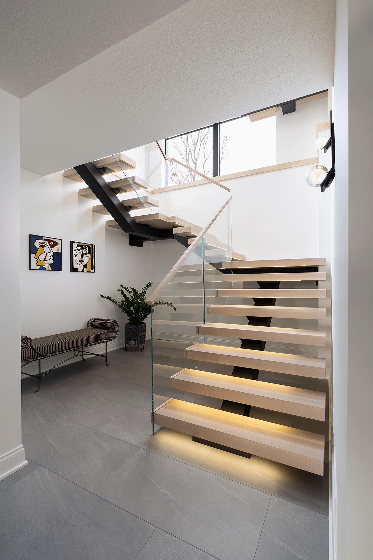 Stair rising from tile flooring with lit treads behind a glass panel