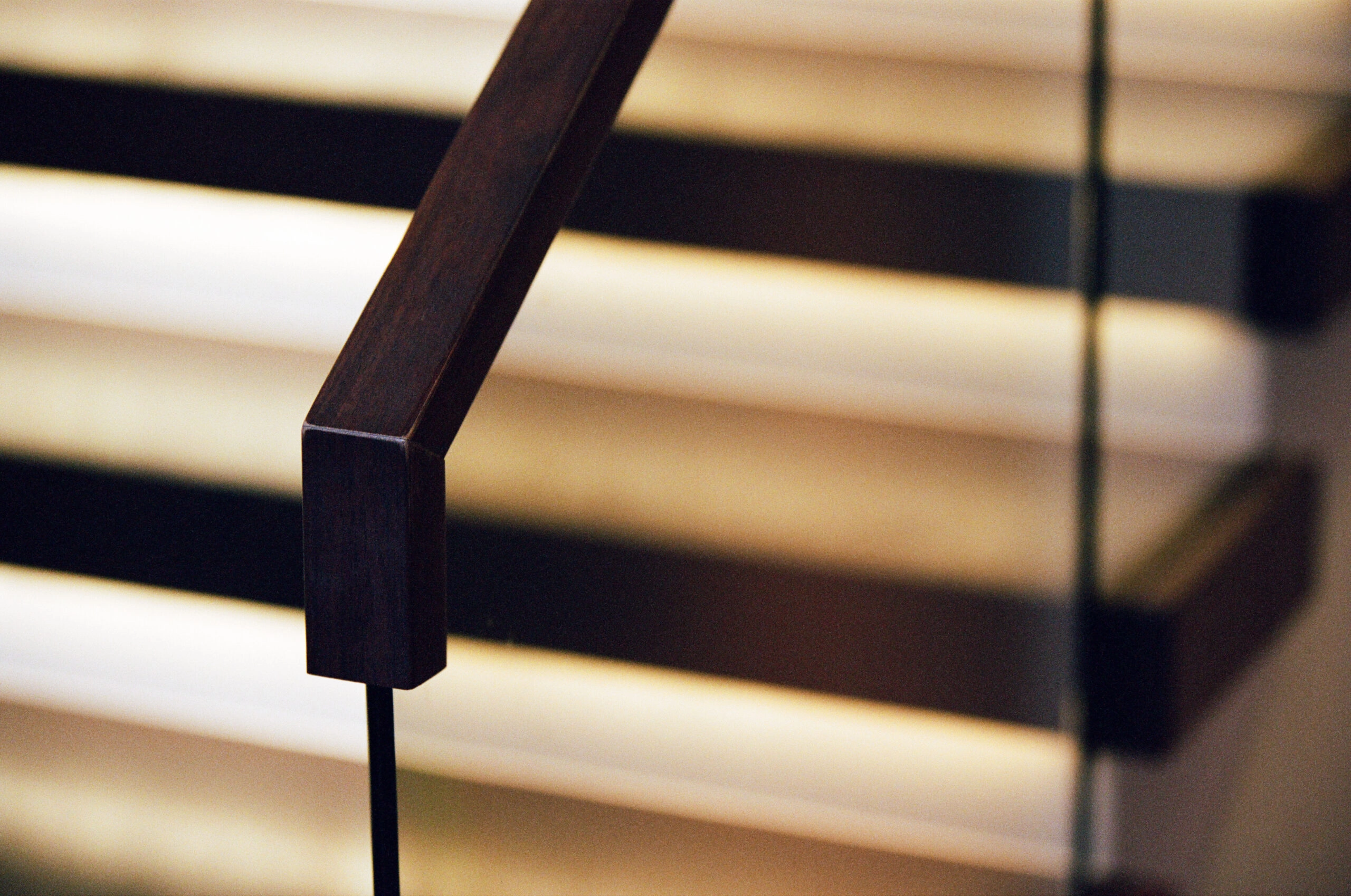 Dark metal handrail cap meeting a slender post with lit treads blurred behind