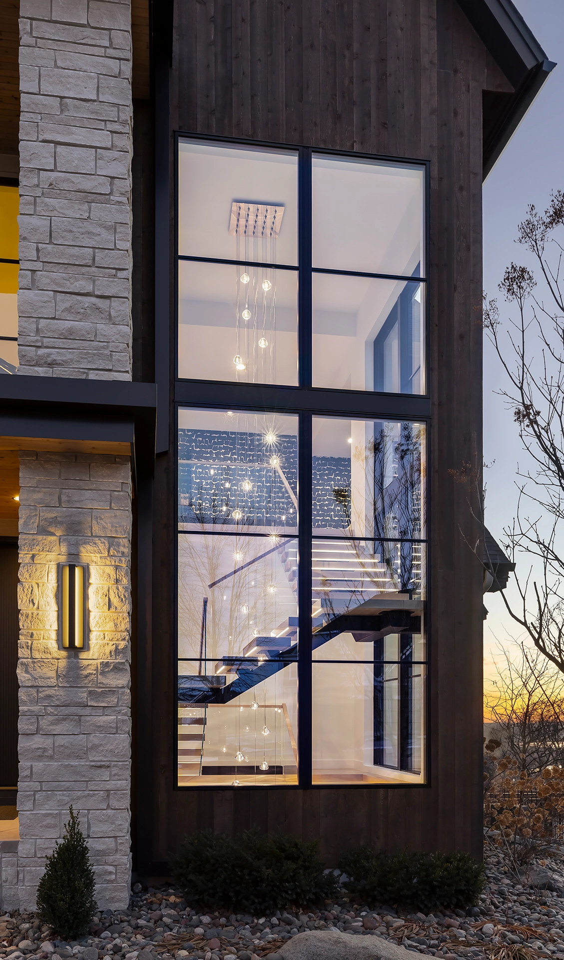 Dusk view from outside where a tall window reveals the lit stair inside