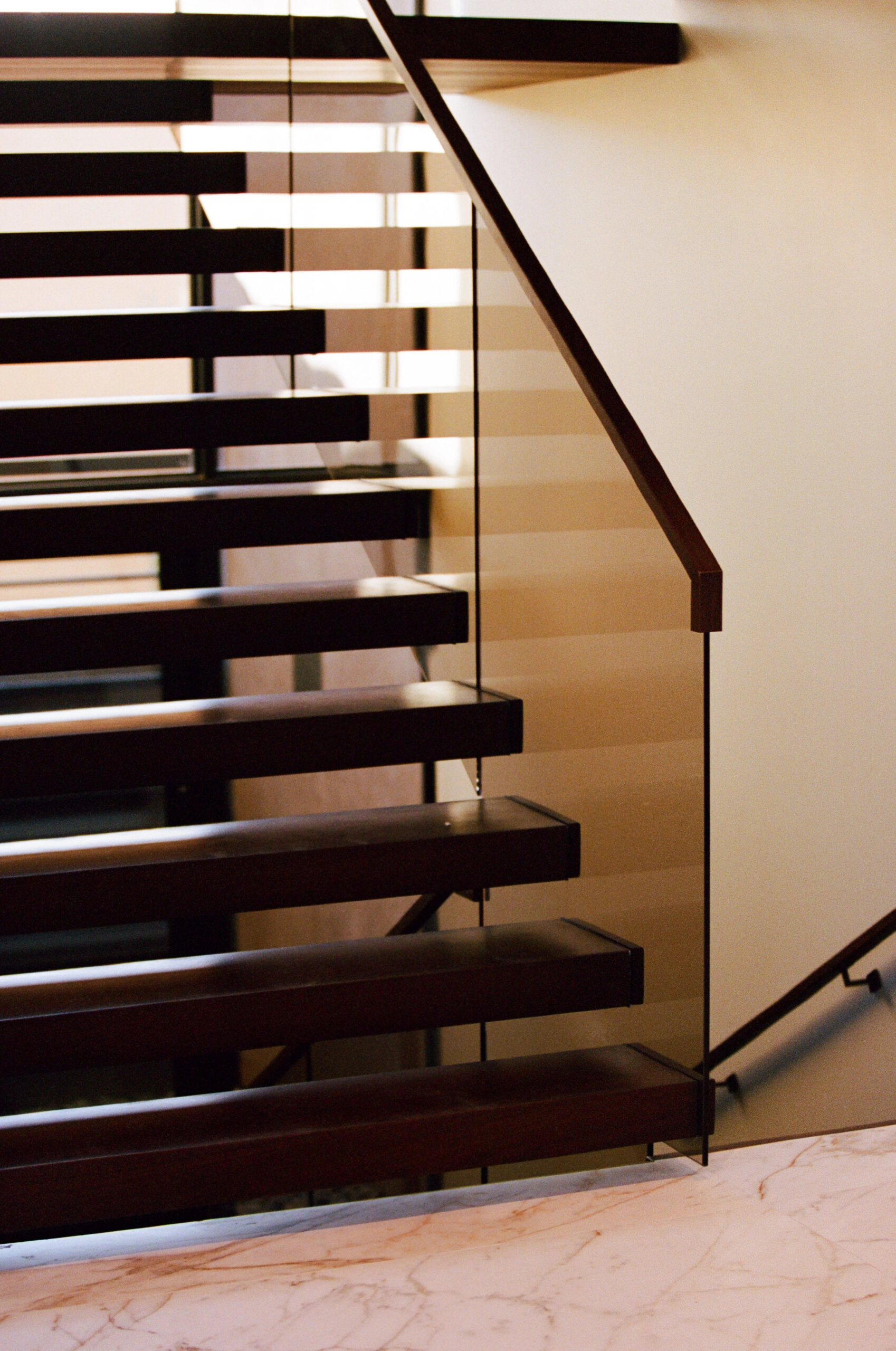 Side view of dark treads and glass railing above a pale marble floor