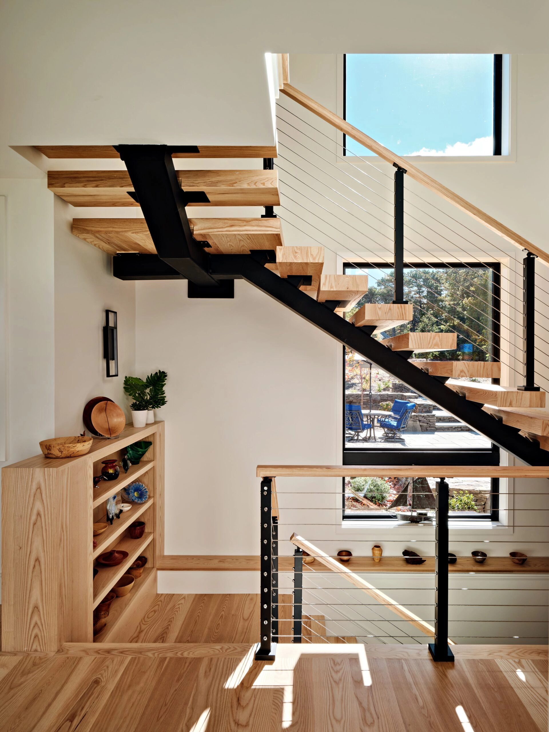 Stair tucked into a nook above built-in shelving, cable railing under a wood rail